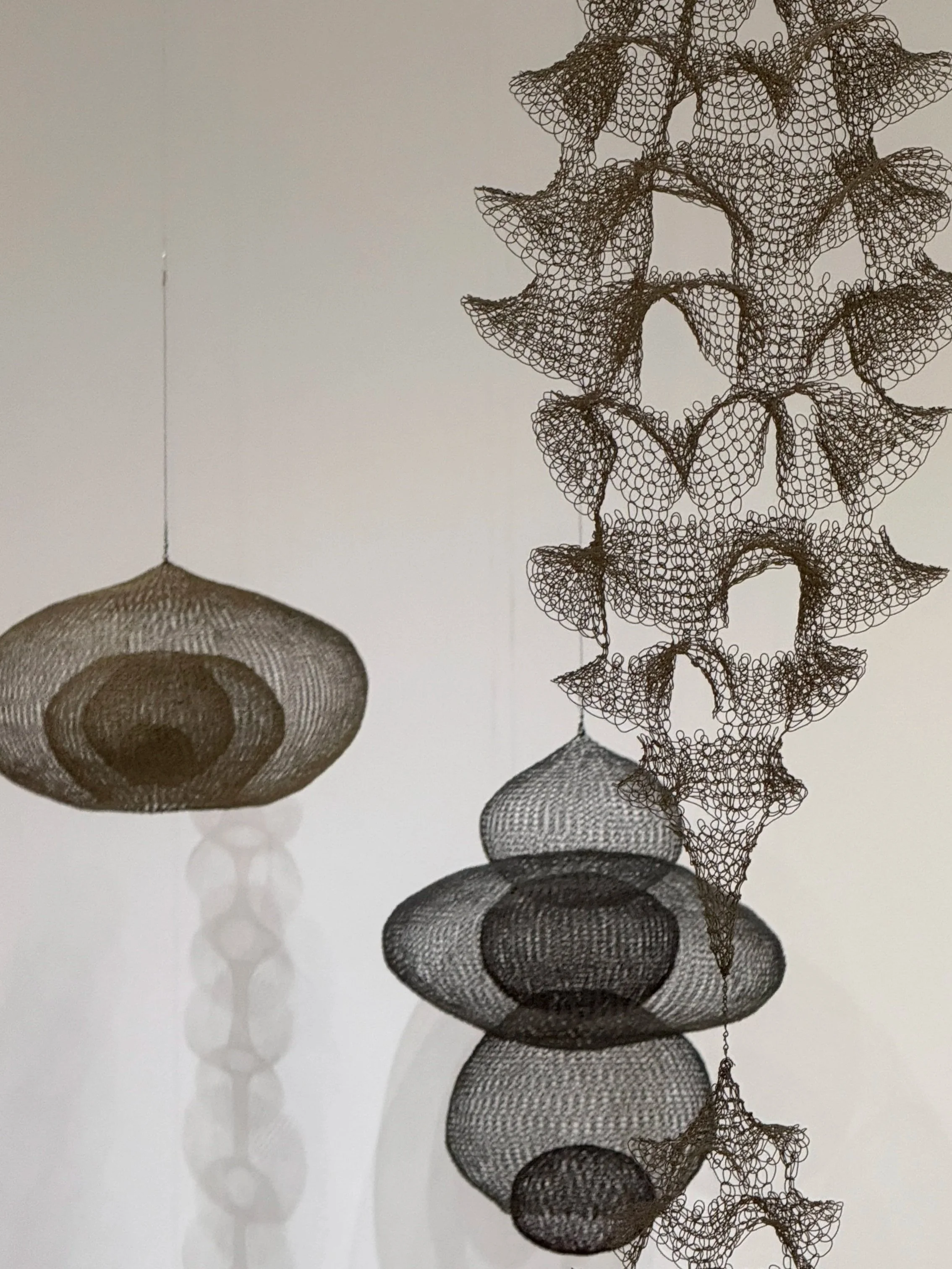 Ruth Asawa wireframe lampshades with intricate, spun metal mesh designs, casting shadows on the wall behind them.