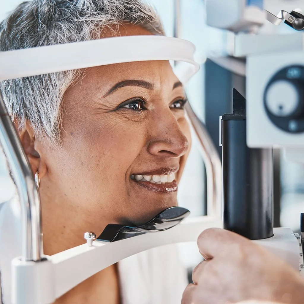 A woman undergoing an eye examination with an optometrist using a phoropter.