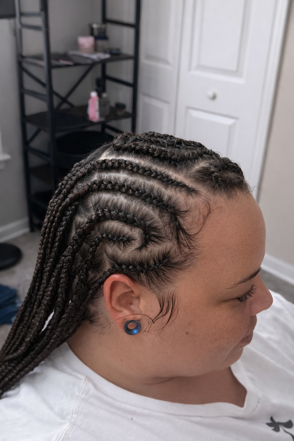 Close-up of a woman with freshly done box braids hairstyle in a room, with a white door and black shelving unit in the background.
