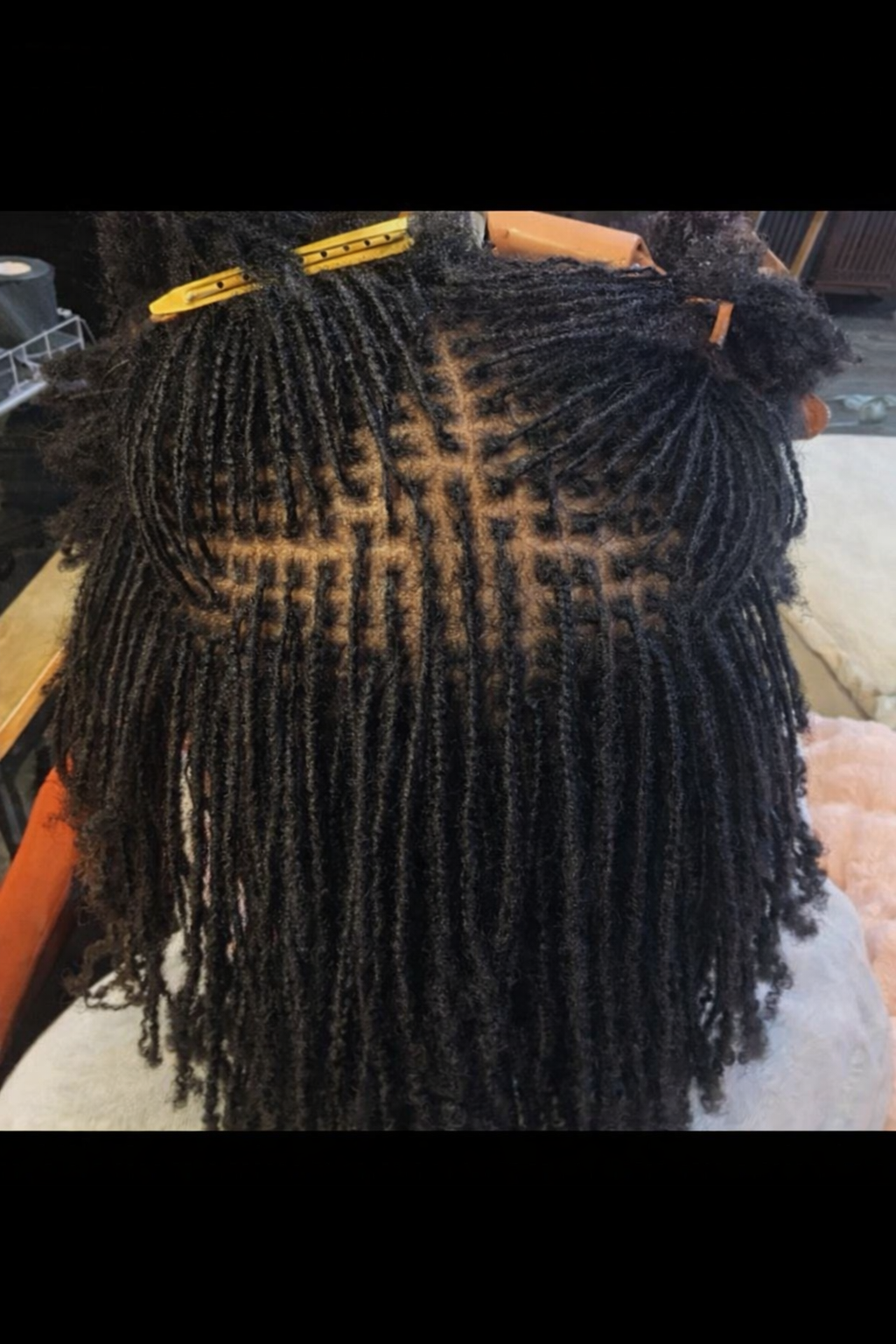 A top view of a person's head with fresh, styled black locs with a pattern shaved into the scalp, secured with yellow clips.