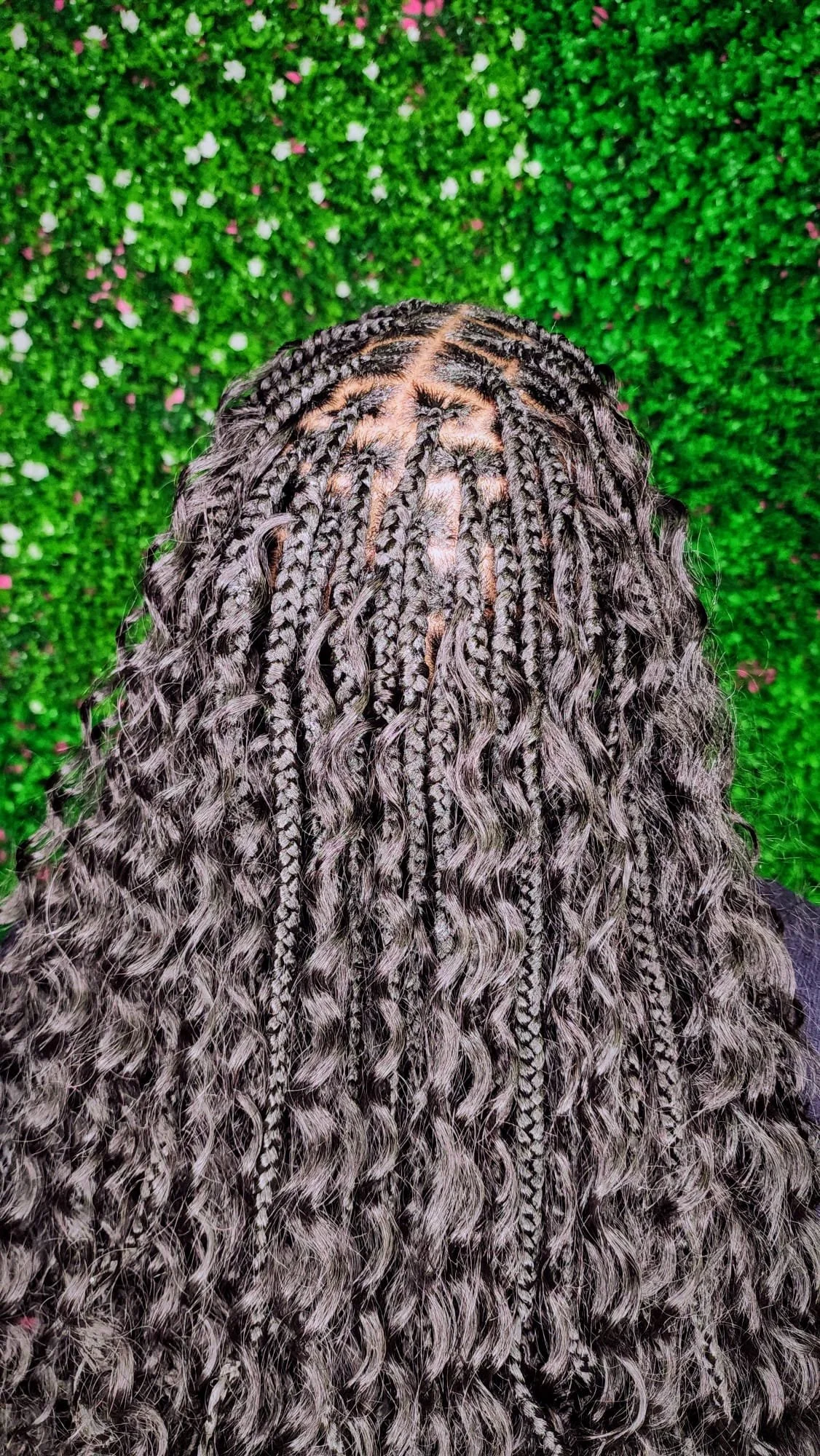 View of long braids with curly ends, viewed from above against a green and pink floral background.
