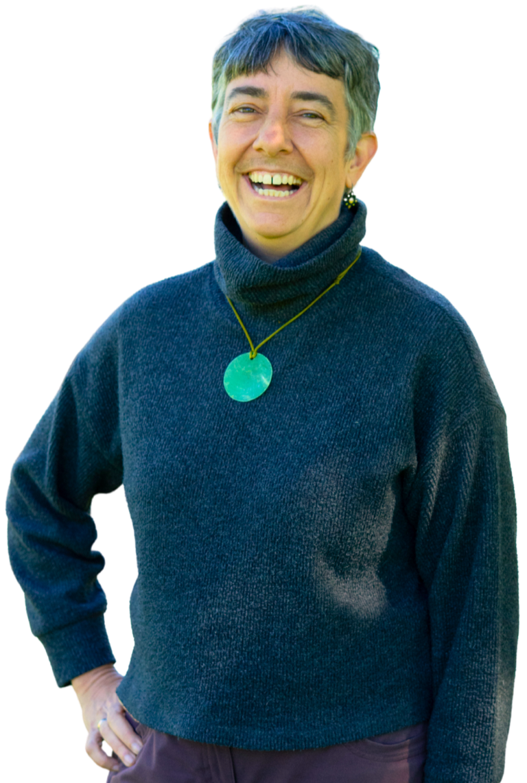 A smiling middle-aged woman with short gray hair wearing a dark turtleneck sweater and a large turquoise pendant necklace.