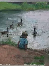 A young child sitting by the water's edge, watching ducks swimming in a pond or lake.