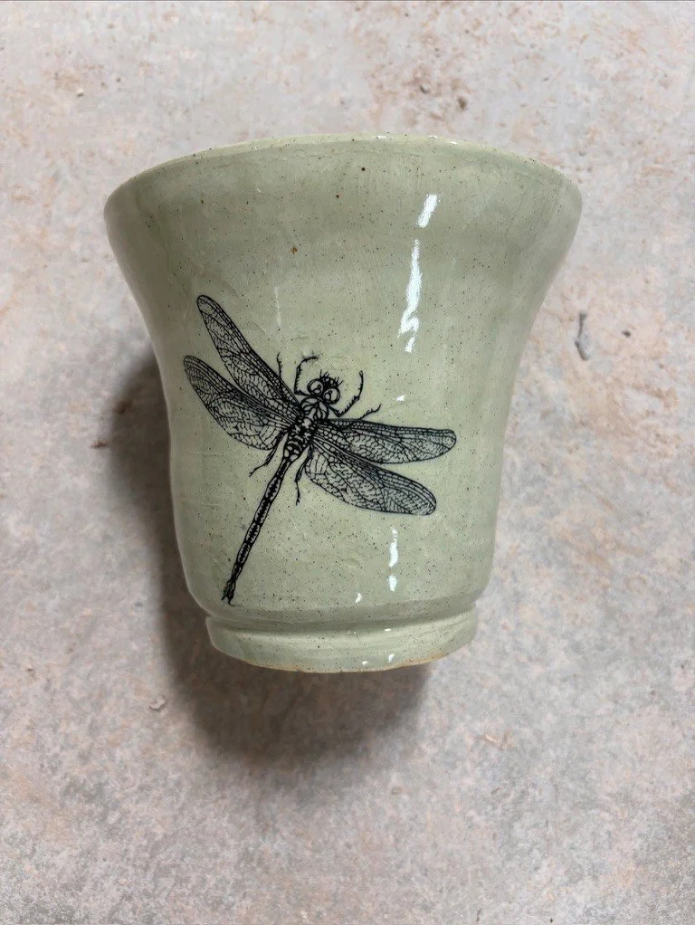 A ceramic cup with a detailed black line drawing of a dragonfly on its surface.