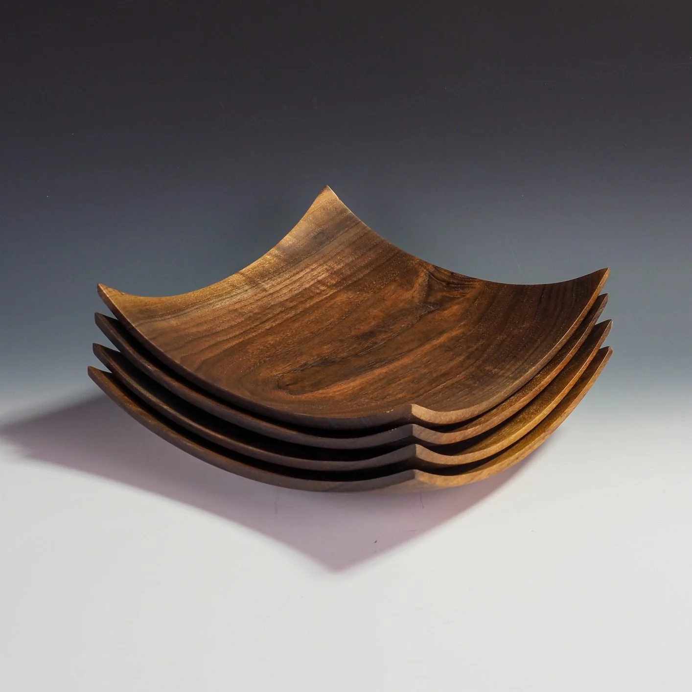 Stack of five wooden bowls with a curved design and dark wood grain pattern, placed on a white and gray gradient background.