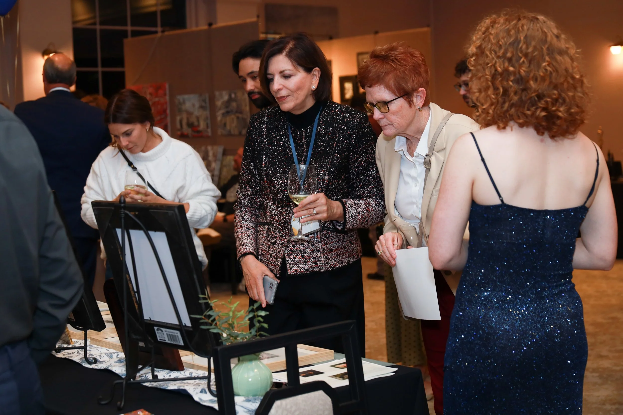 People attending an art or craft exhibition, viewing displayed artwork and products on a table.