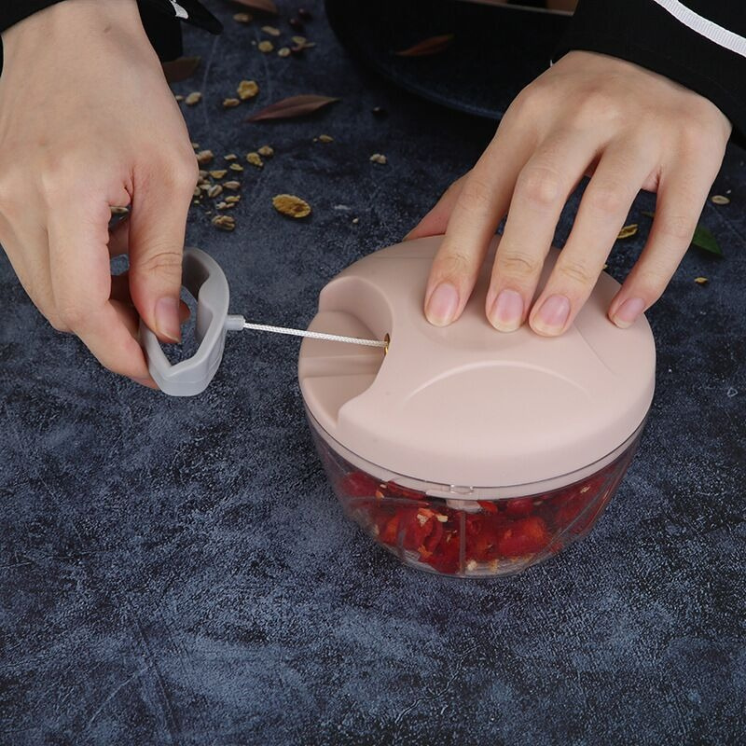 Hands using a manual pull string food chopper to chop ingredients inside a clear bowl