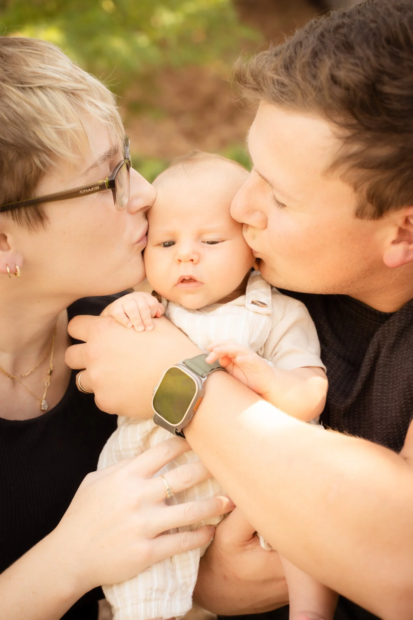 A family moment where a woman and a man are kissing a baby on the cheeks.