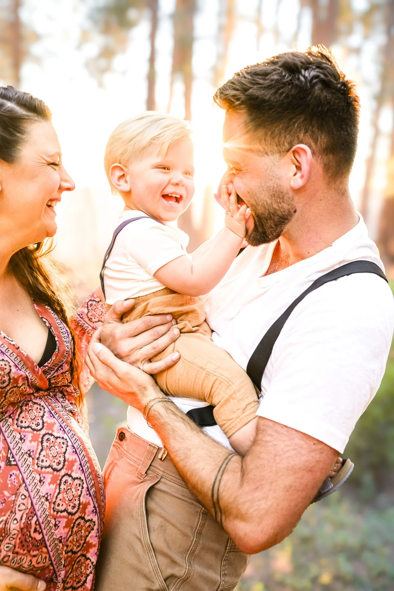 A smiling family outdoors during daytime, with a man holding a laughing young boy and a woman smiling beside them.