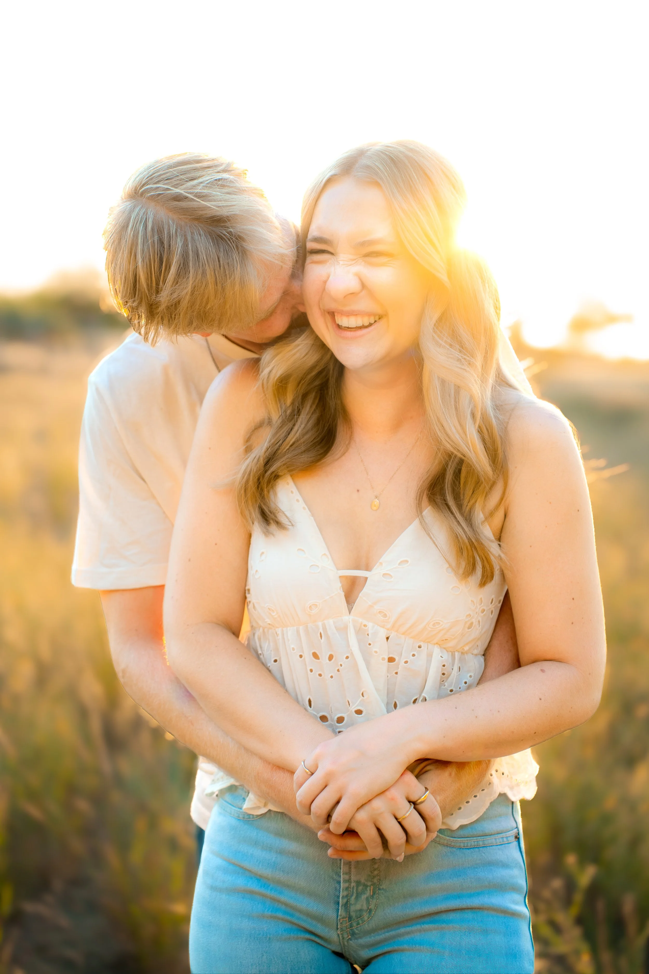 Two women sharing a joyful moment outdoors at sunset, one whispering to the other, both smiling, with a natural landscape background during a couples session in Bidwell Park in Chico, CA.