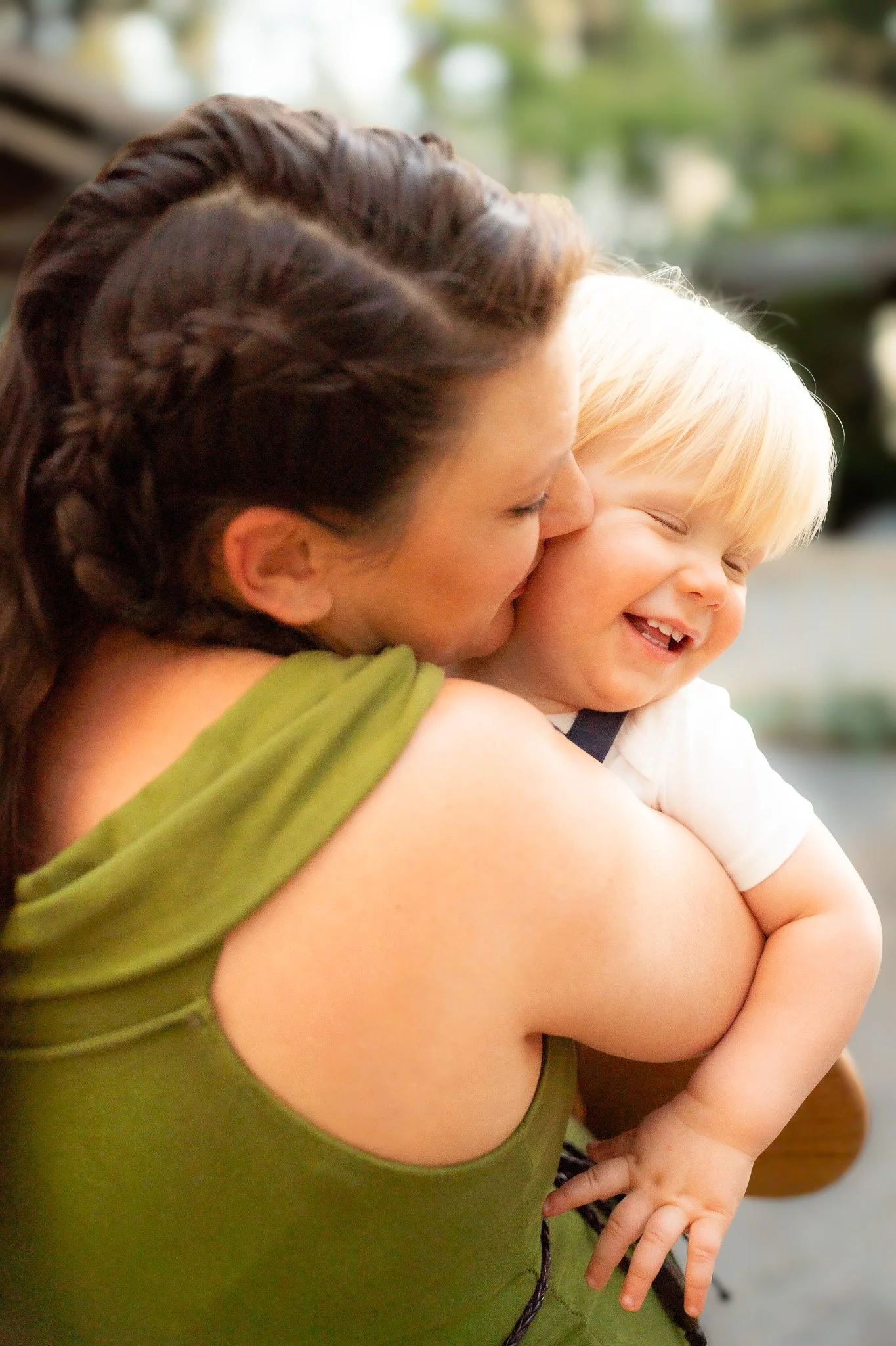 A woman with braided hair holding a smiling young boy with blond hair in an embrace.