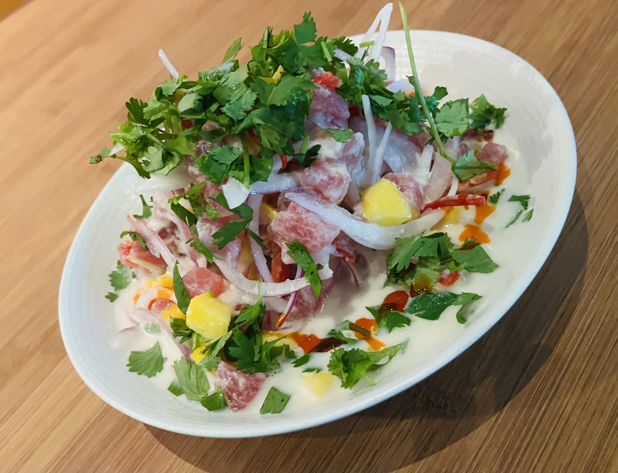 A bowl of ceviche garnished with cilantro, served on a wooden table.