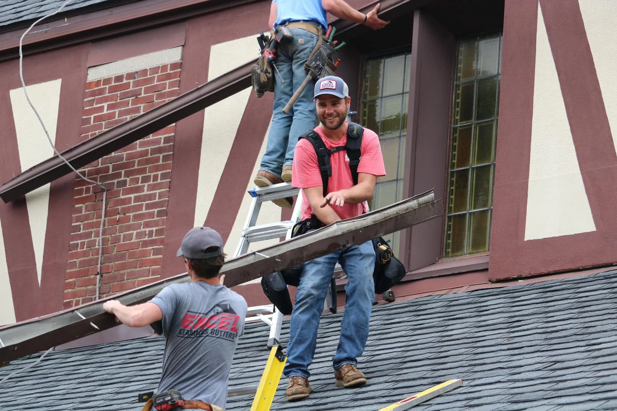 Workers on a ladder repairing or installing an awning on the side of a building with brick and stucco exterior.
