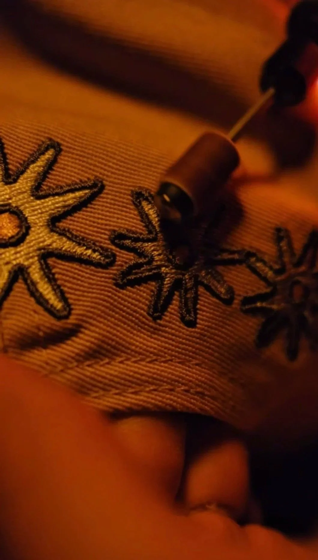 Close-up photo of embroidered flowers on fabric, with a small container and a sewing pin resting on it.
