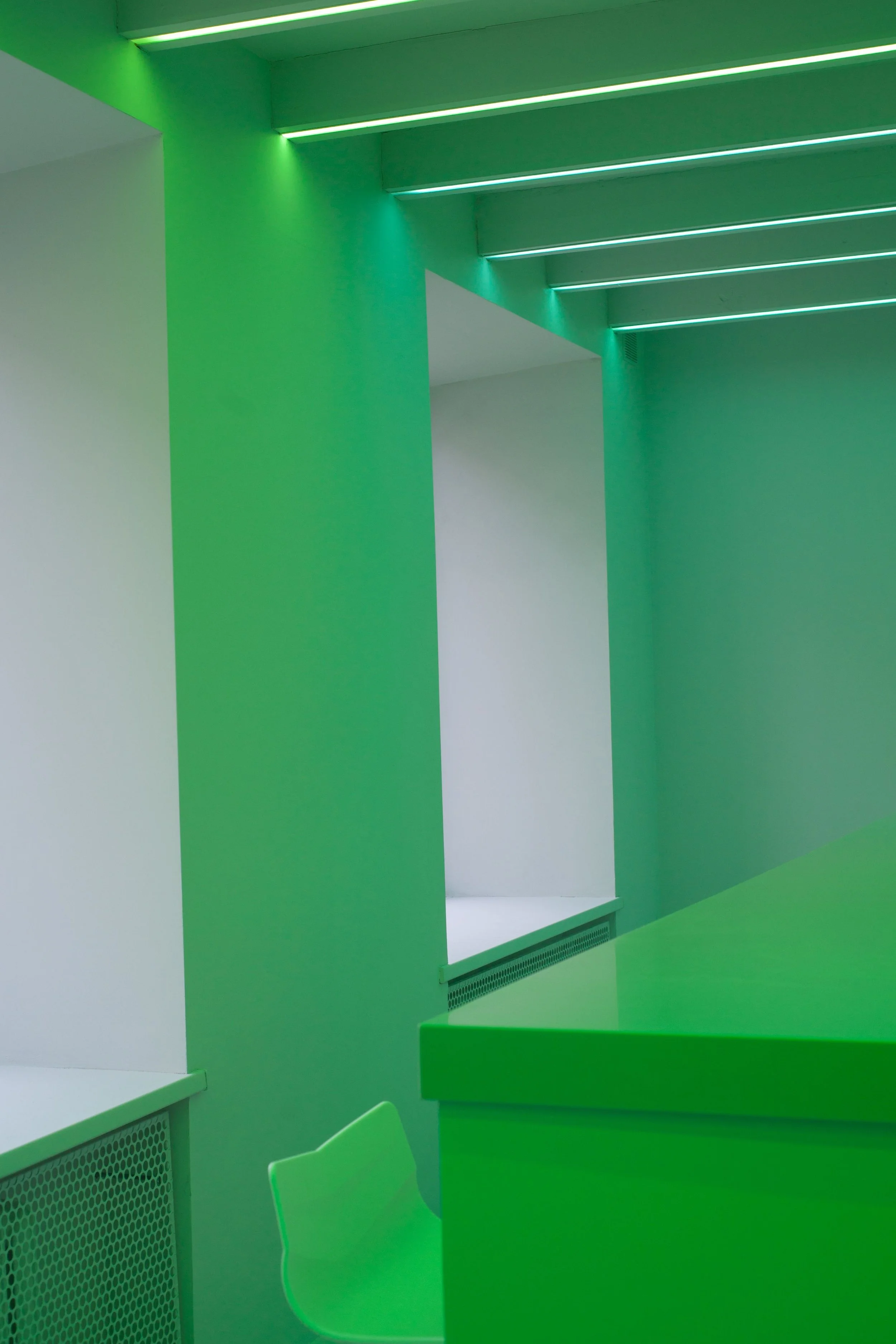 Interior of a modern room, branded with bright green walls and ceiling, featuring LED strip lighting, a white window sill, and green furniture.