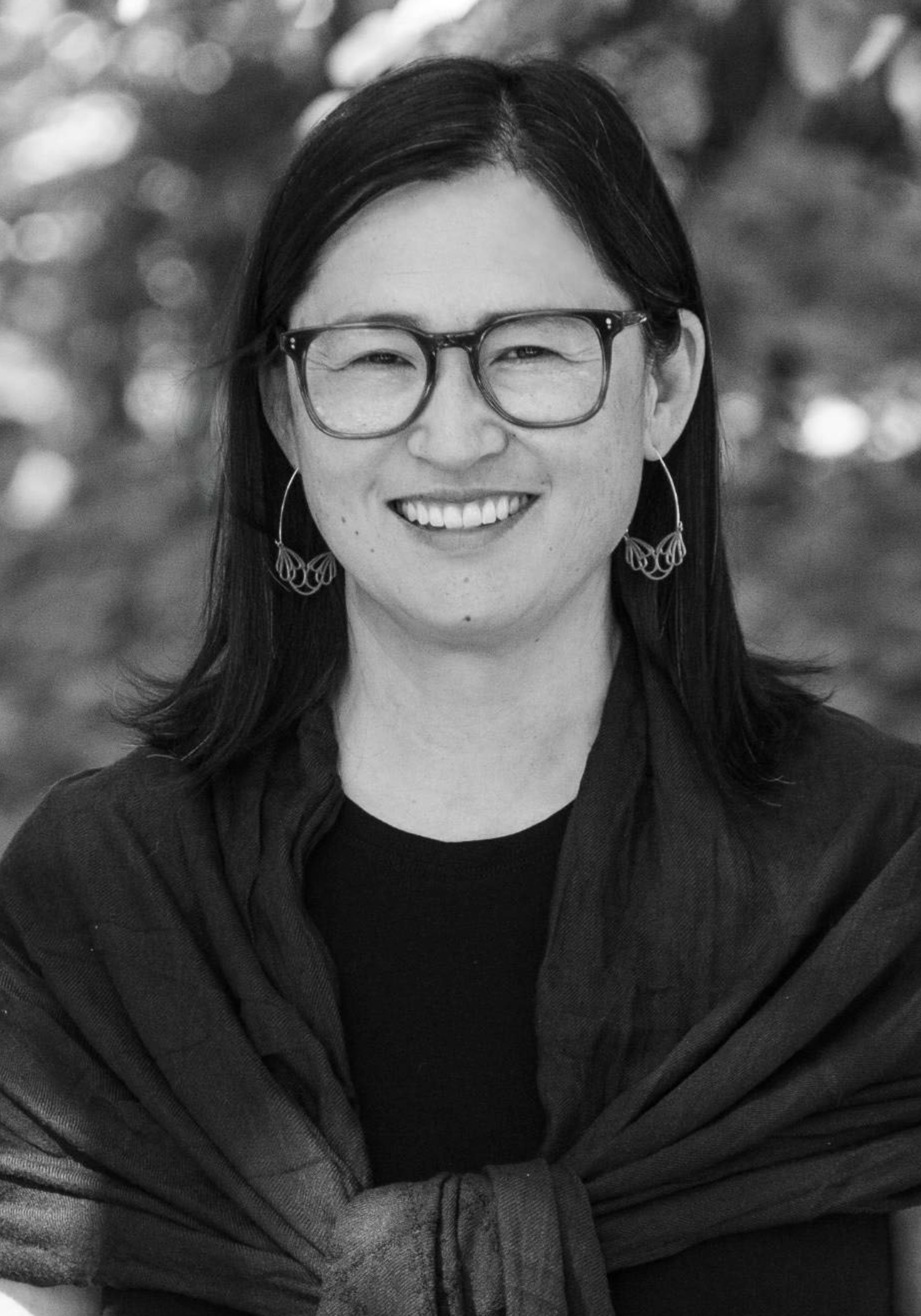 A black and white photograph of Sandy Park, smiling with glasses, wearing earrings, and wrapped in a scarf.