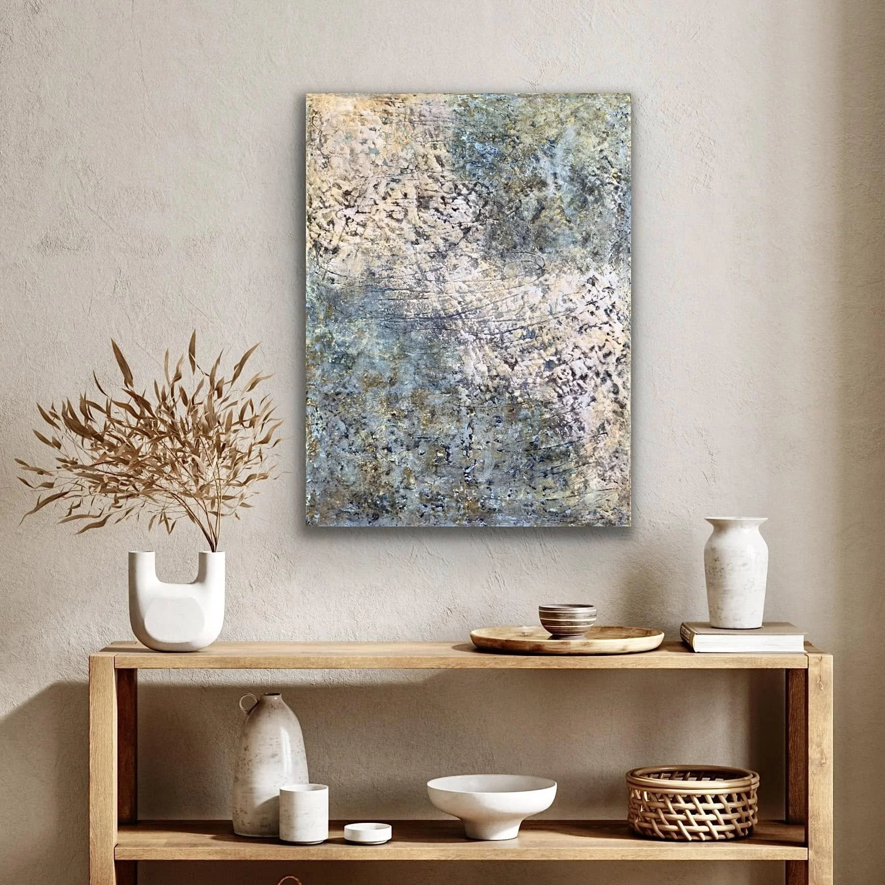 Decorative interior scene with a wooden table, white vases, dishes, and a woven basket, with a large abstract painting on a beige wall.