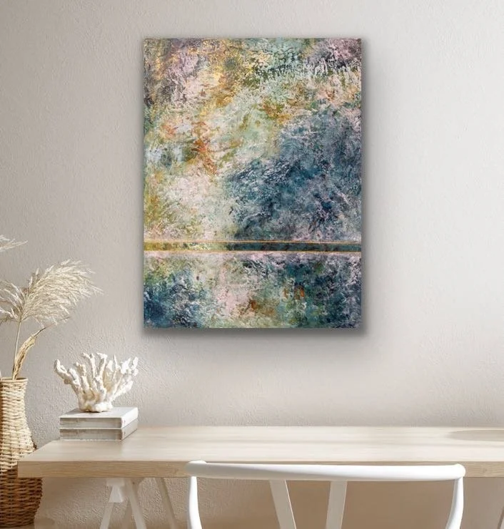 Abstract watercolor art in shades of blue, green, purple, and gold hanging on a white wall above a minimalist desk.