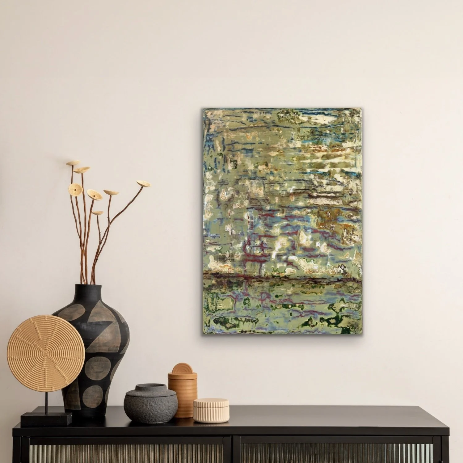 Modern interior decor with a black sideboard, abstract painting, decorative vases, a woven basket, and a tall vase with artichoke-shaped branches on a white wall.