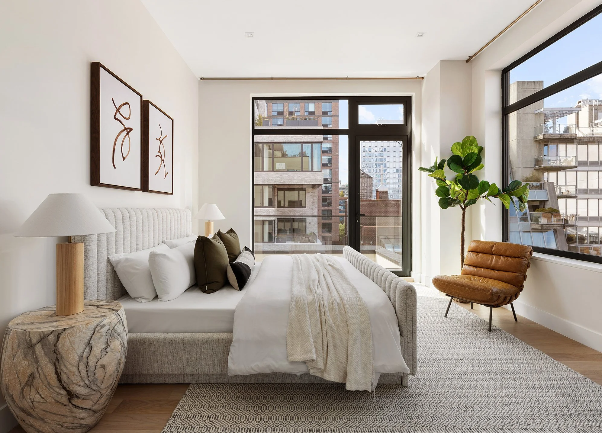 Staging art direction - Modern living room with large windows, a white upholstered bed, lamps, abstract wall art, a potted plant, and a leather armchair.