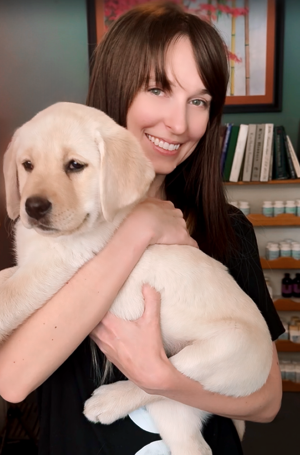 Westside Acupuncture business manager, Hailey Dowling, smiles brightly holding a cute yellow Labrador puppy.