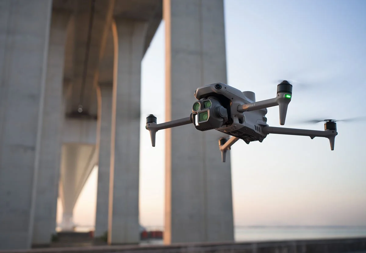 A drone flying under a concrete bridge at sunset.