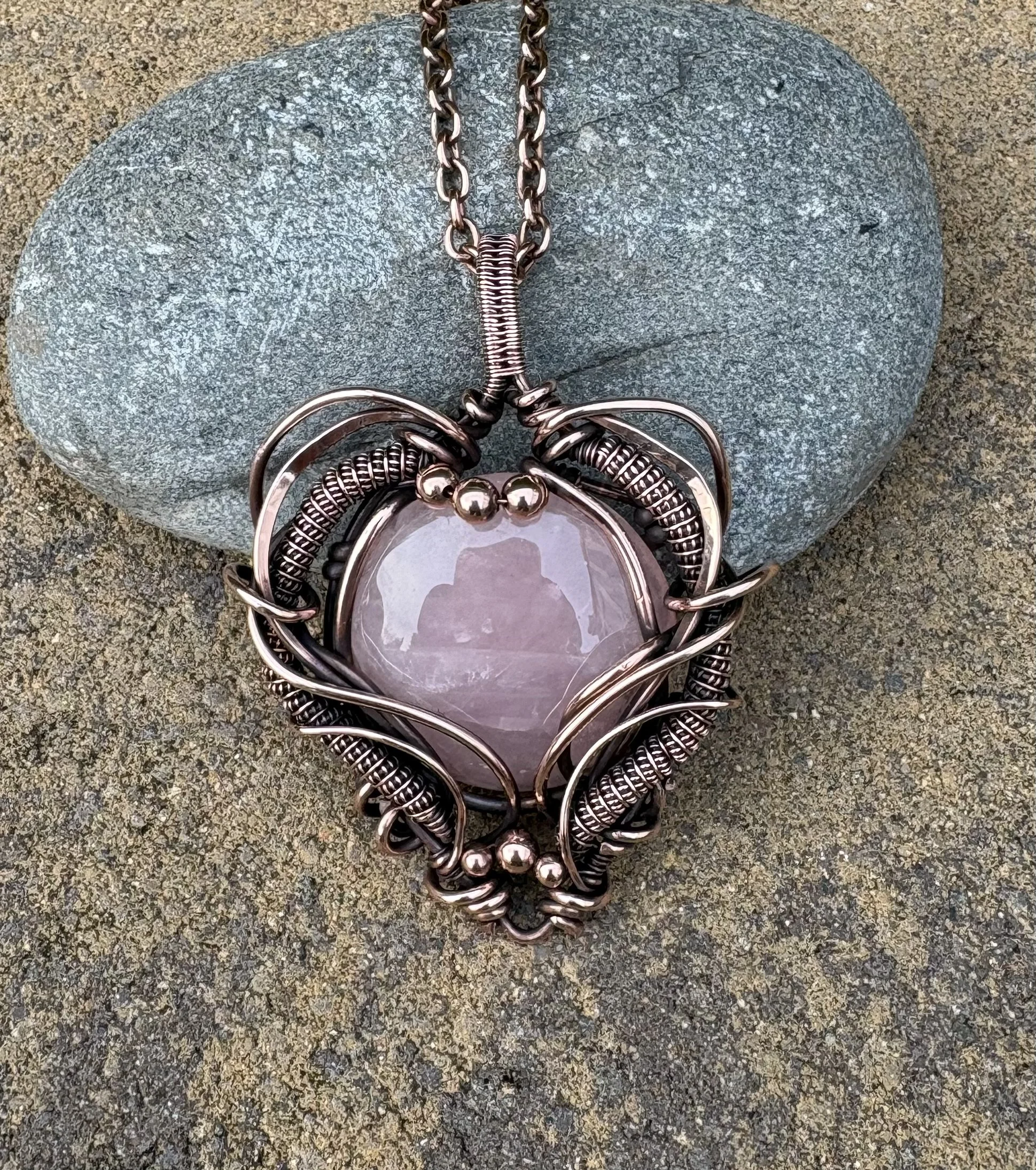 A large decorative mirror with a metallic, wireframe edge resting on a rock. The mirror has a rounded top and is surrounded by metallic details, resembling an ornate frame.