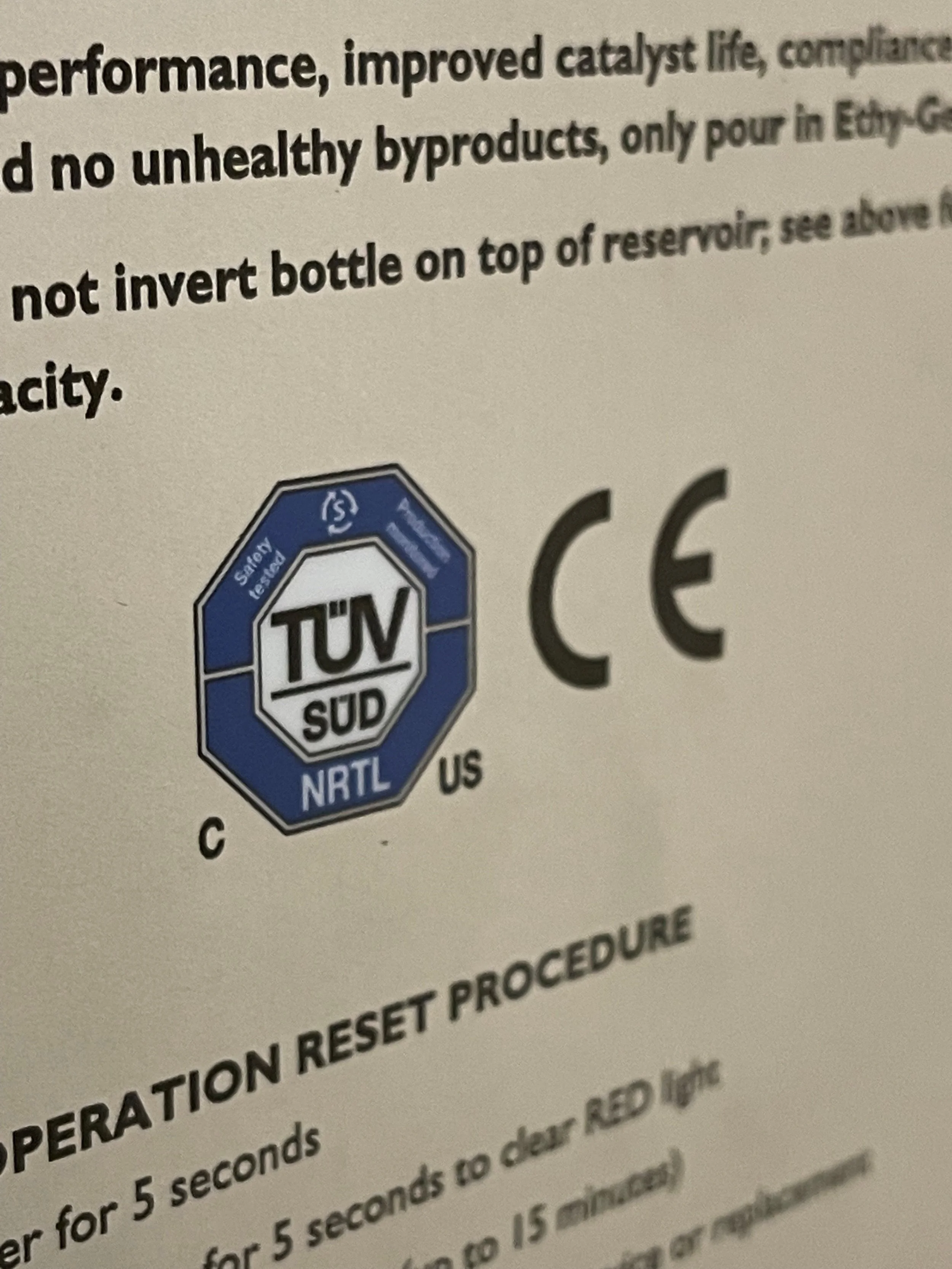 Close-up of a label with safety certifications including TÜV SÜD and CE marks, along with text about operation reset procedures.