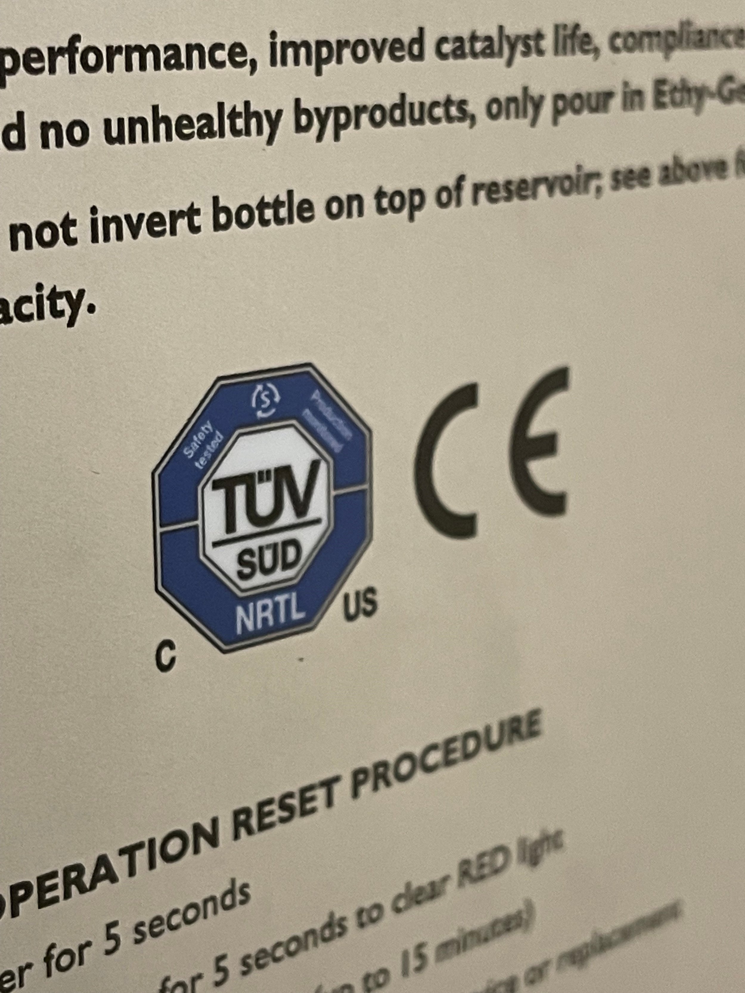 Close-up of a label with safety certifications including TÜV SÜD and CE marks, along with text about operation reset procedures.