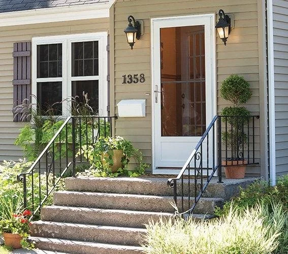 Front entrance of a house with stairs, a white door with glass panels, potted plants, and house number 1358.