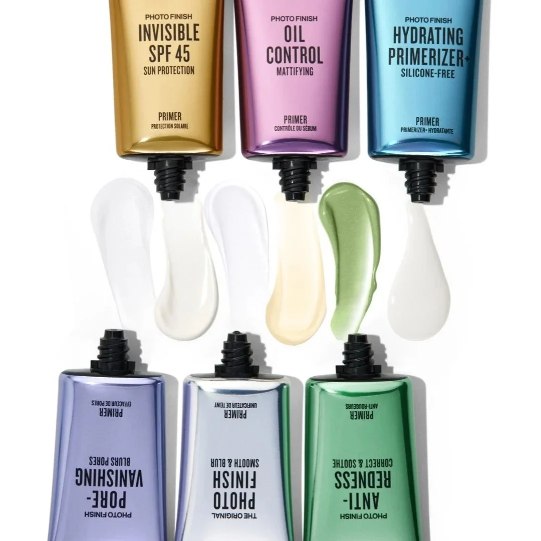Six tubes of skincare primer, each with a different label and color, with some of the primer squeezed out below.
