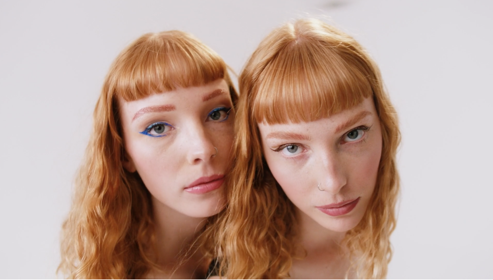 Two young women with red hair and light skin, posing close together against a plain gray background.