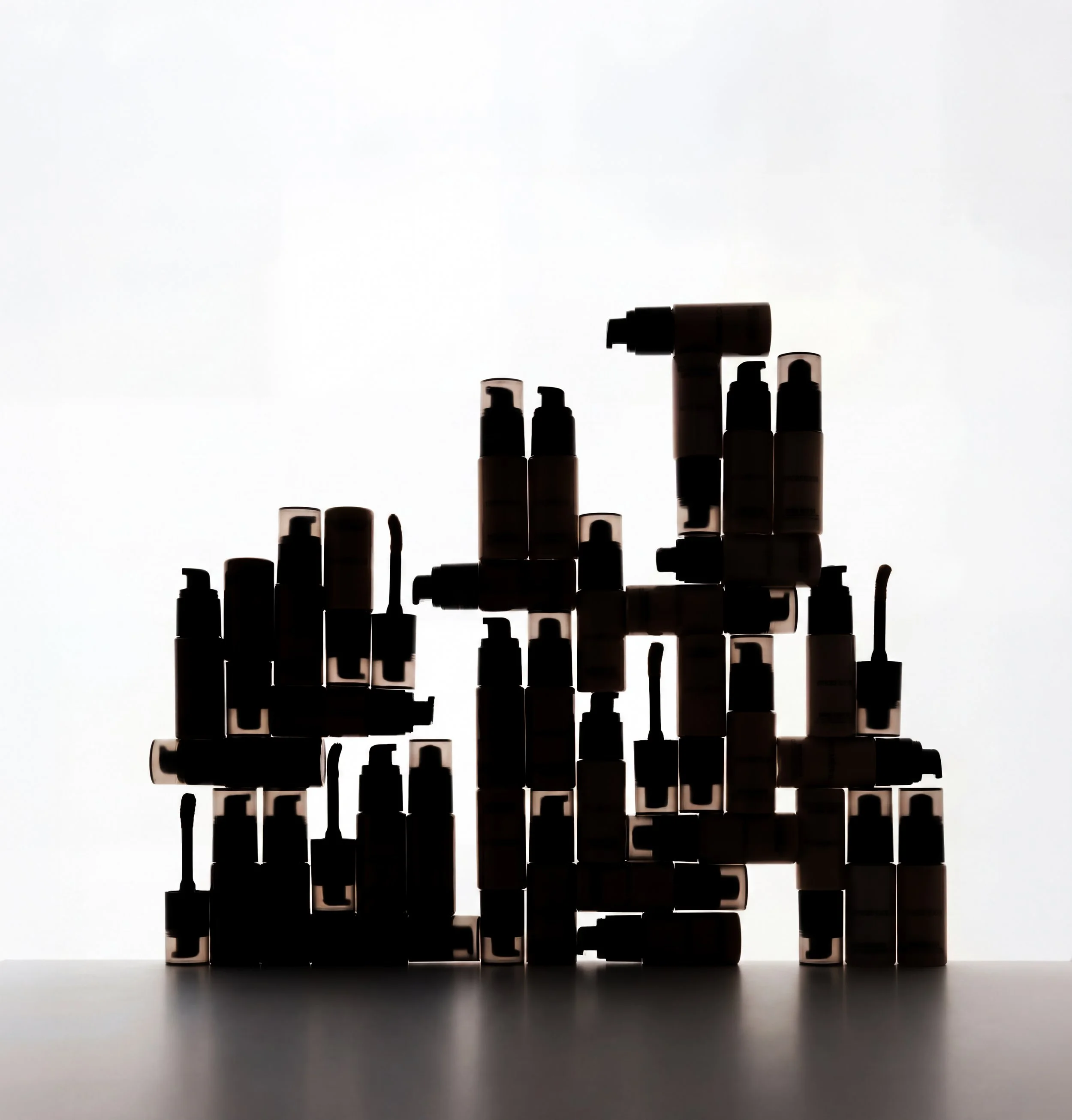 Silhouettes of various spray bottles on a flat surface, with a bright light background