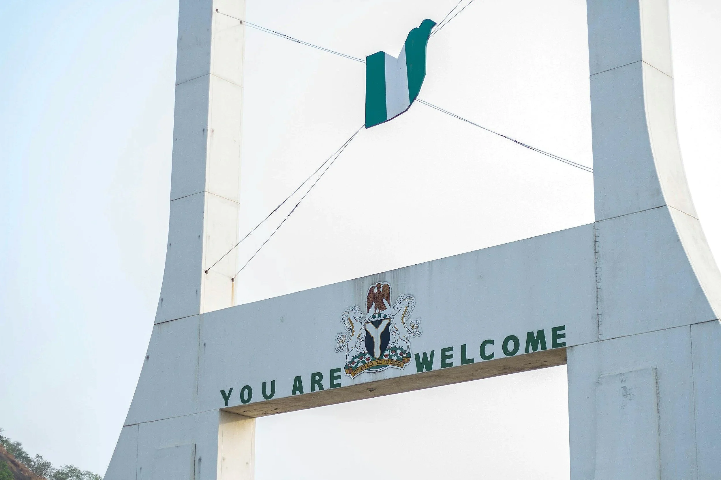 A large white signboard with a coat of arms featuring a red eagle and two white unicorns, and the words 'WELCOME YOU ARE'