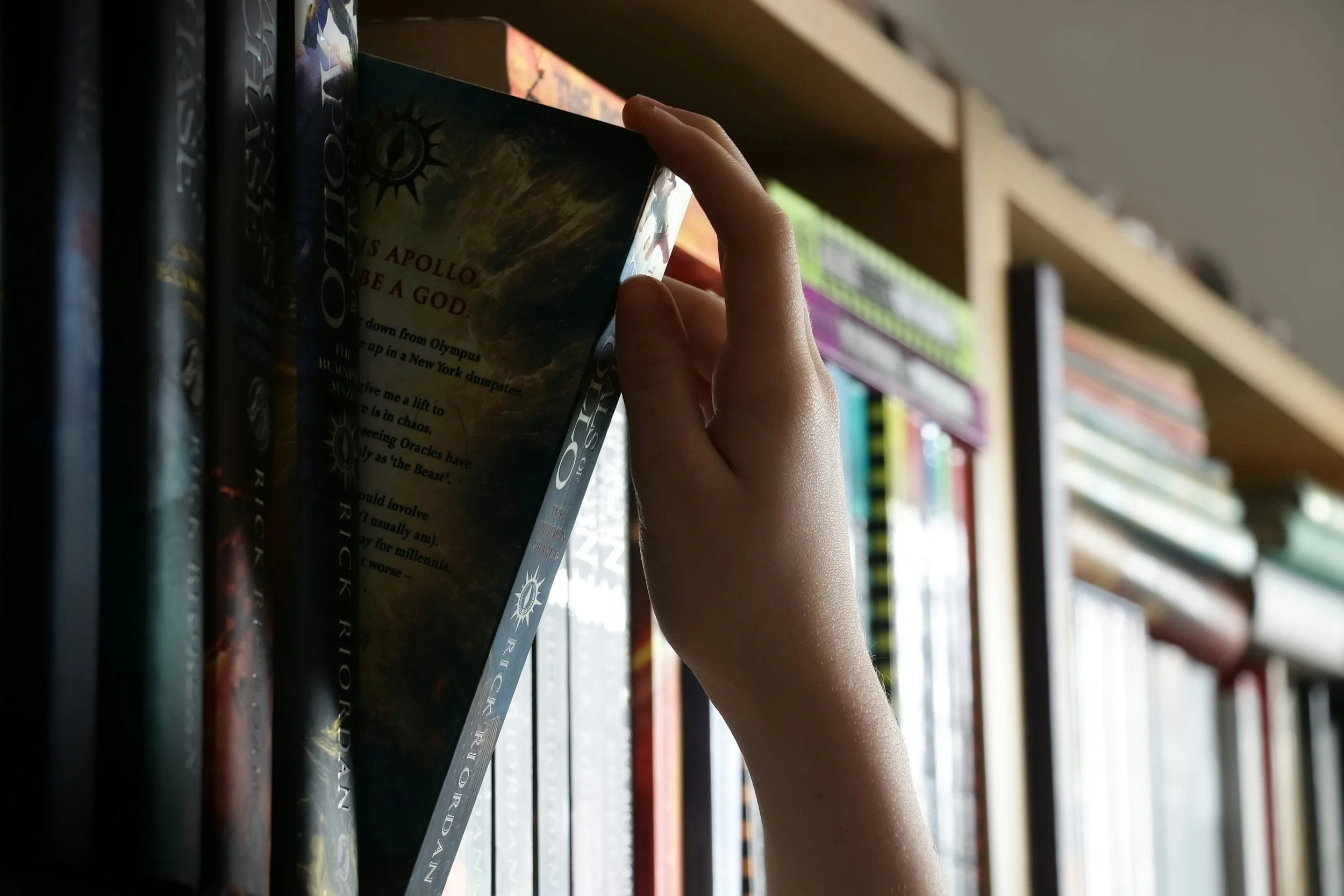 A person's hand is reaching for a book titled 'APOLLO' on a bookshelf filled with books in various colors and sizes.