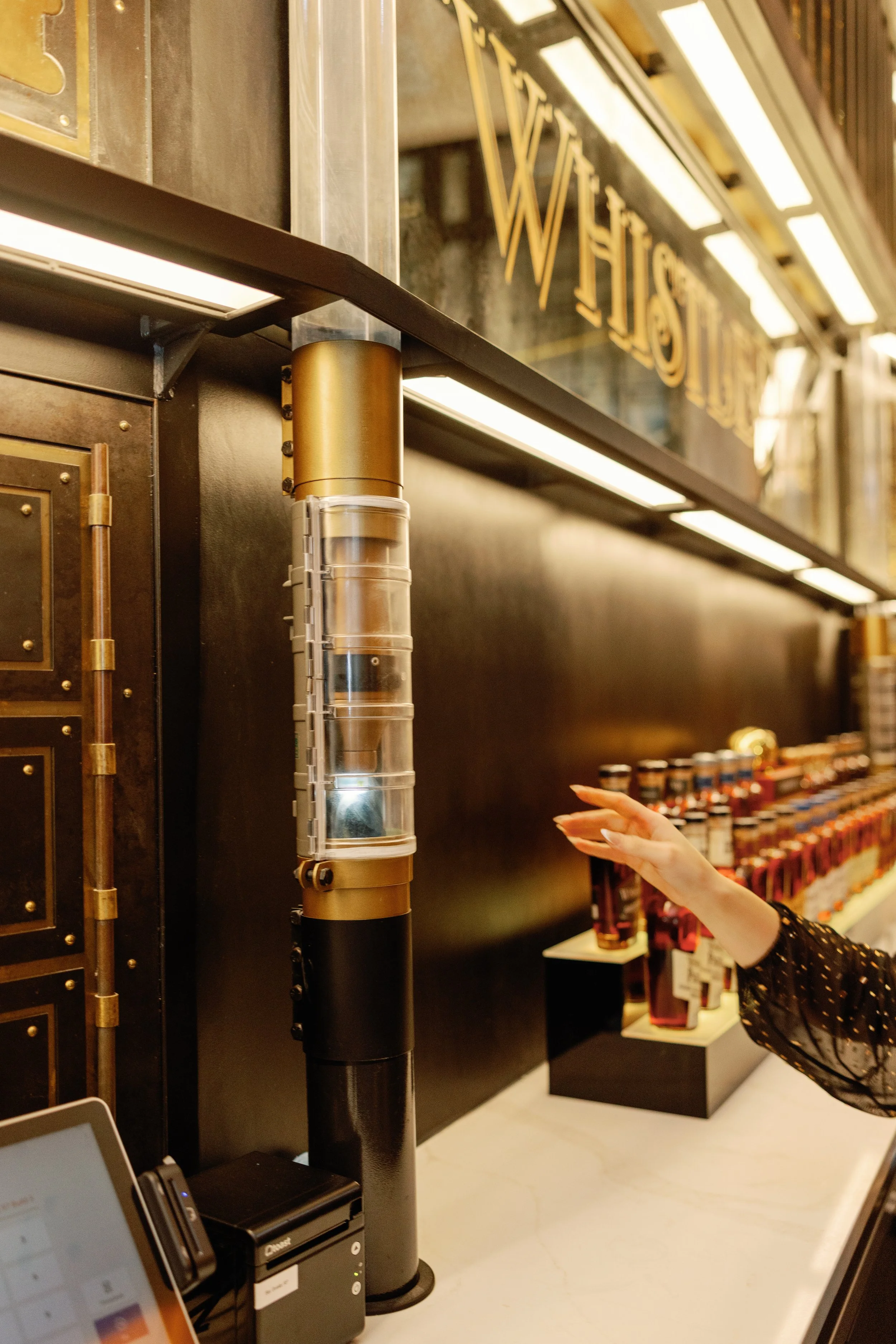 A person reaching out towards the flying cocktail delivery system on a counter, in a store or bar with shelves of bottles in the background.