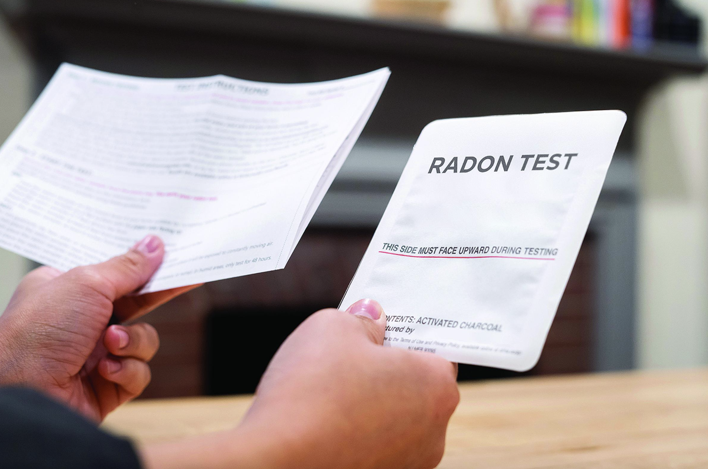 Person holding a saliva sample collection tube and a sheet labeled 'Radon Test' with instructions for testing.