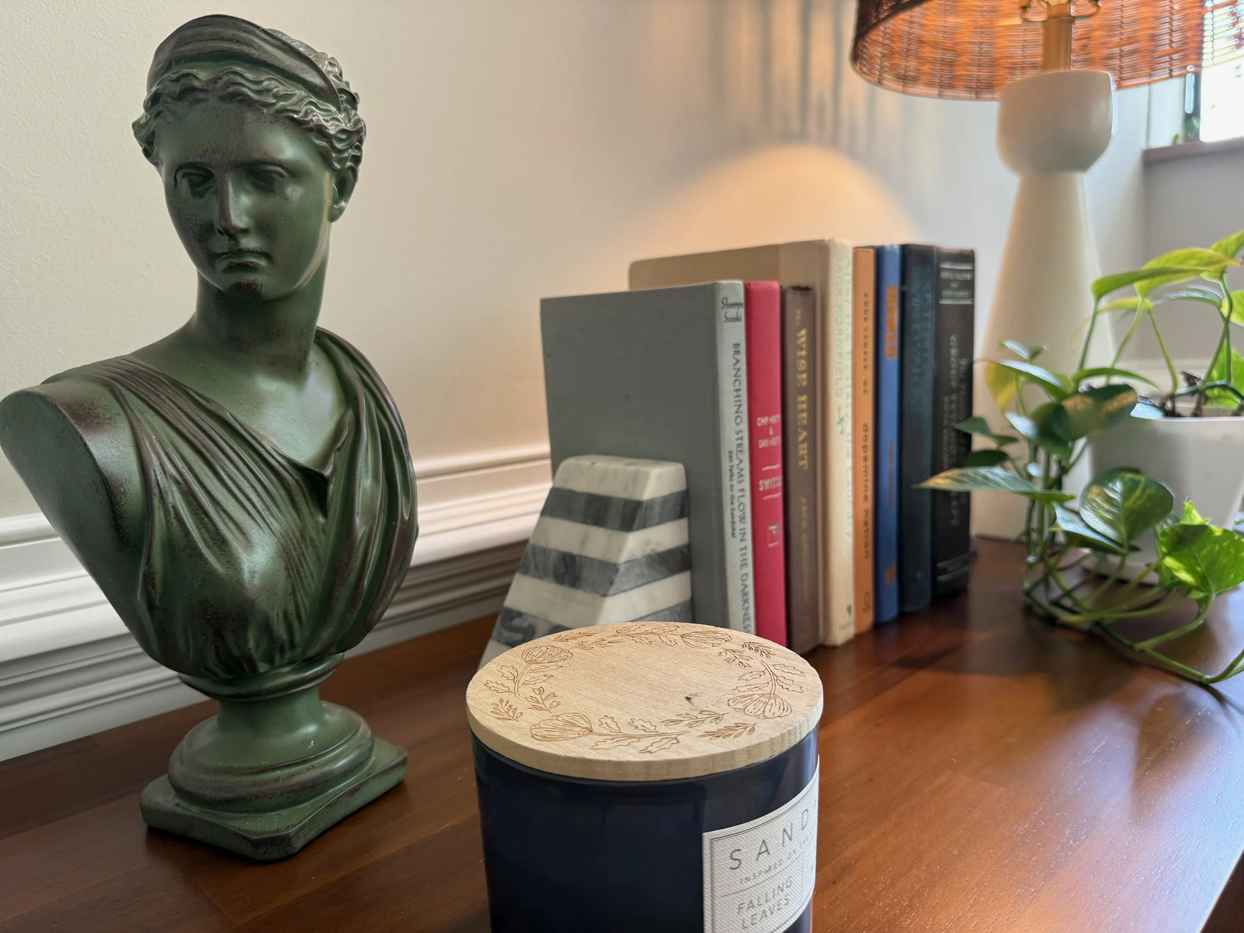 Decorative bust of a woman on a shelf next to books and a potted plant in a well-lit room.