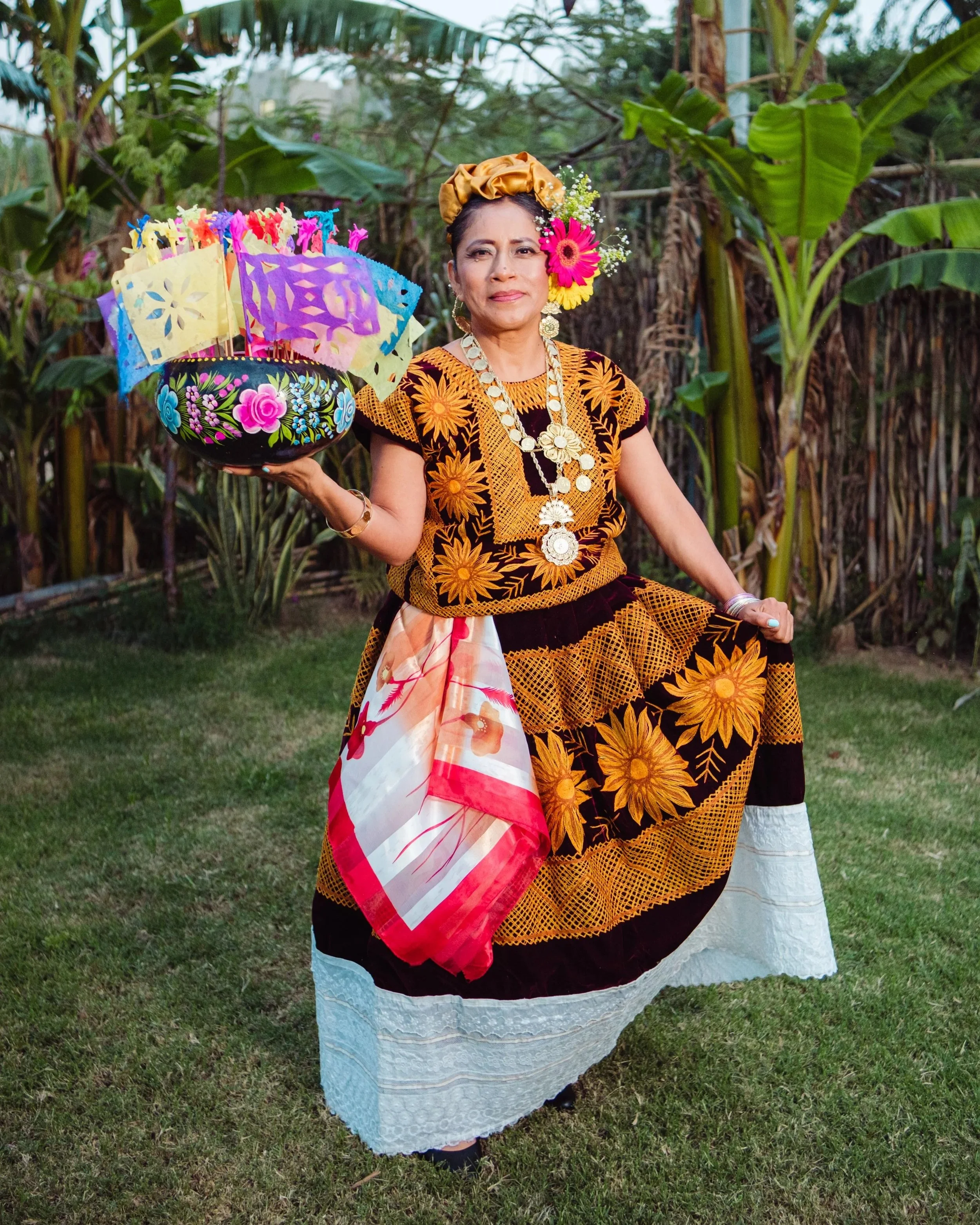 Woman in traditional Oaxacan dress holding a hand-painted gourd with papel picado flags