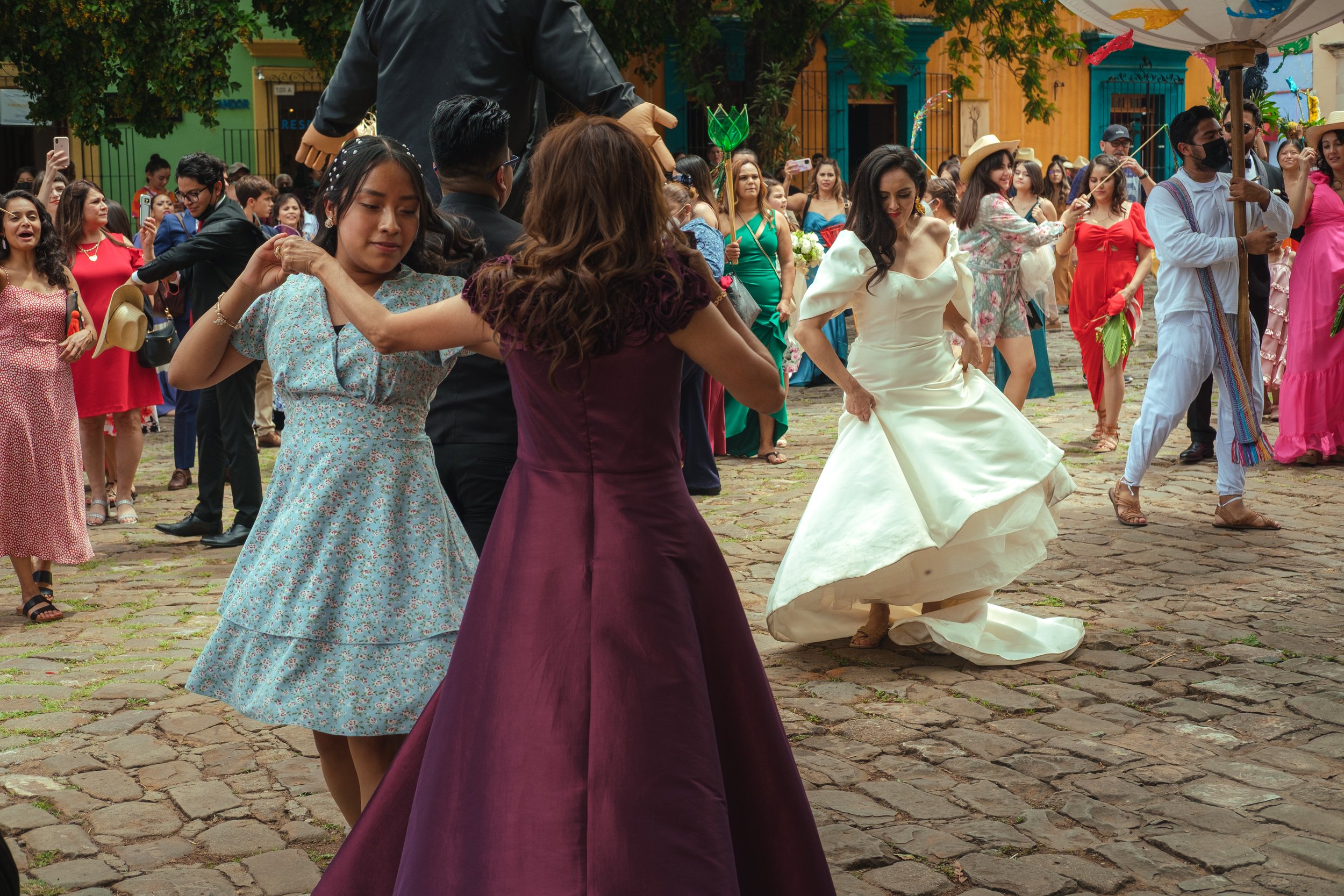 People dancing and celebrating outdoors in a calenda in oaxaca many women in colorful dresses and a woman in a white gown