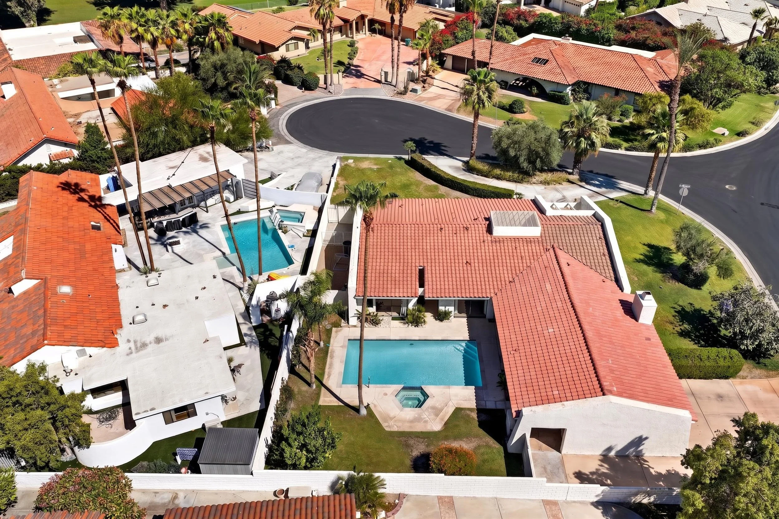 Bird's-eye view of a residential neighborhood with houses, a cul-de-sac, palm trees, and a swimming pool.