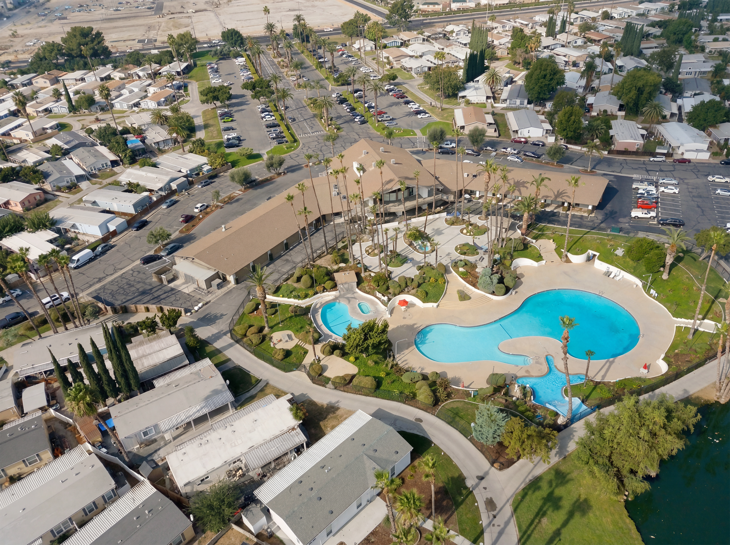Aerial view of a residential area with houses, palm trees, parking lots, and a large swimming pool with a decorative shape and a small pool for children.