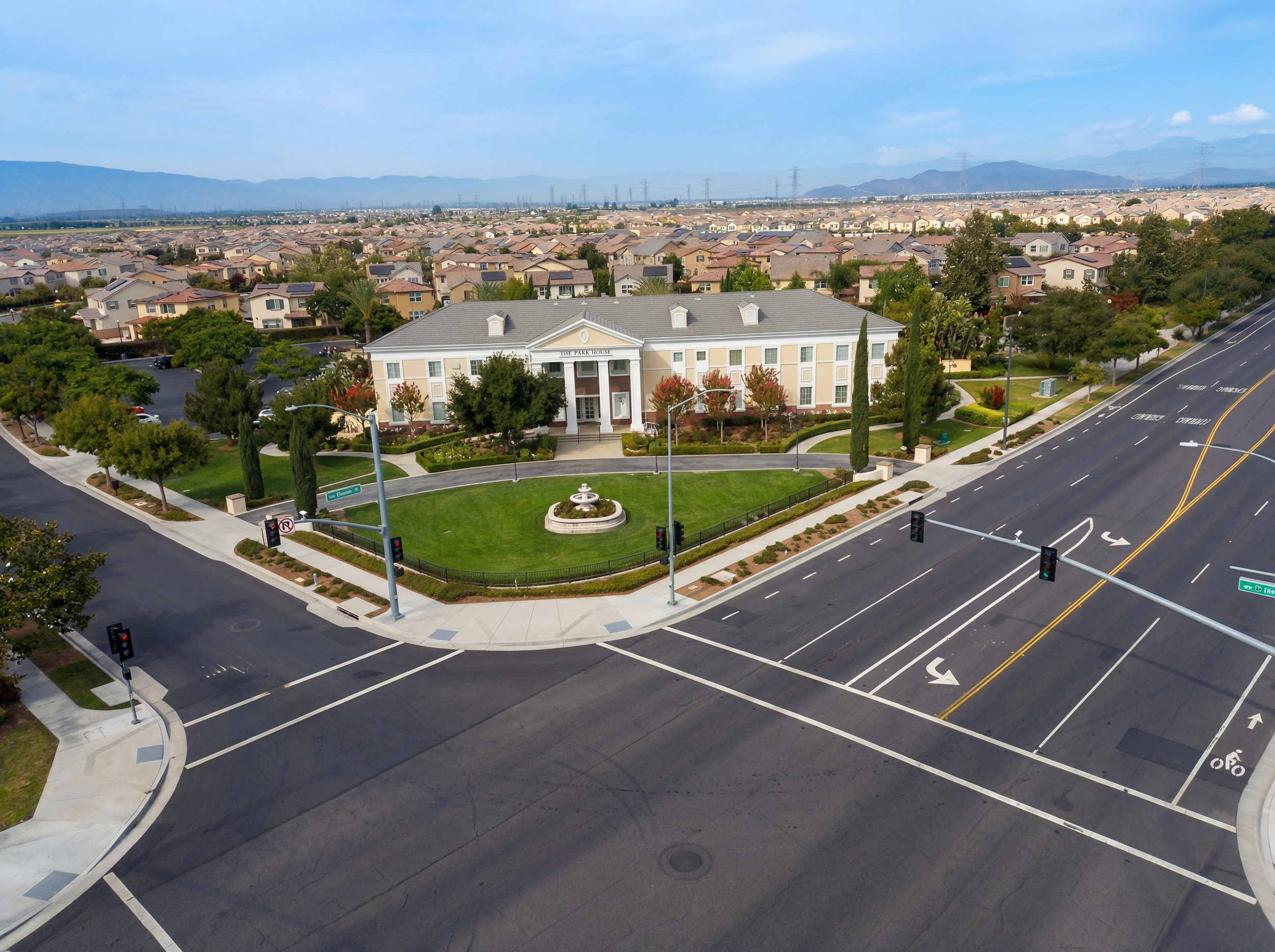 Aerial view of a suburban neighborhood with houses, trees, and streets, with a large building labeled 'The Park House' in the foreground, and mountains in the background.