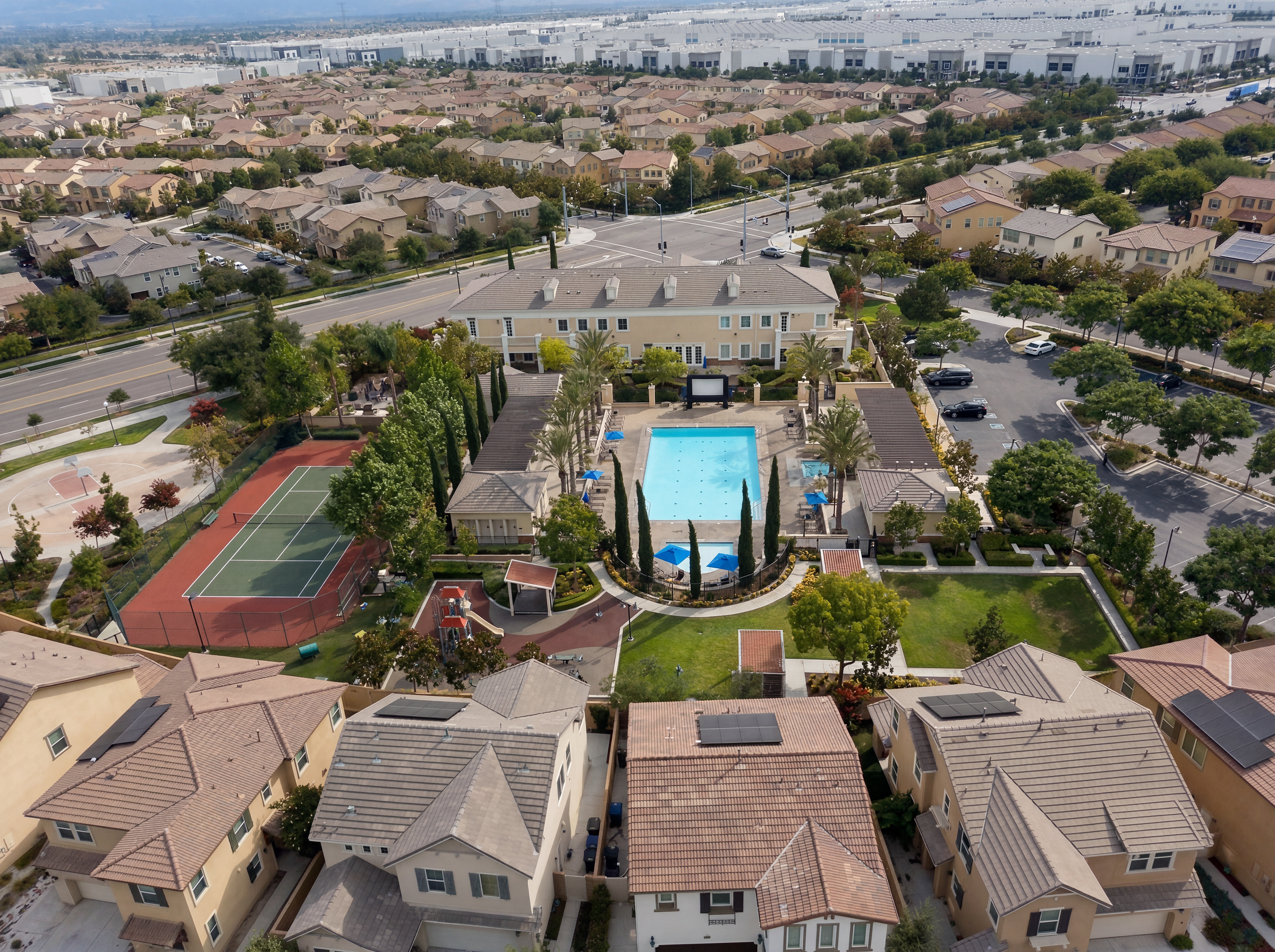Aerial view of a residential neighborhood with houses, trees, streets, a swimming pool, and a tennis court.