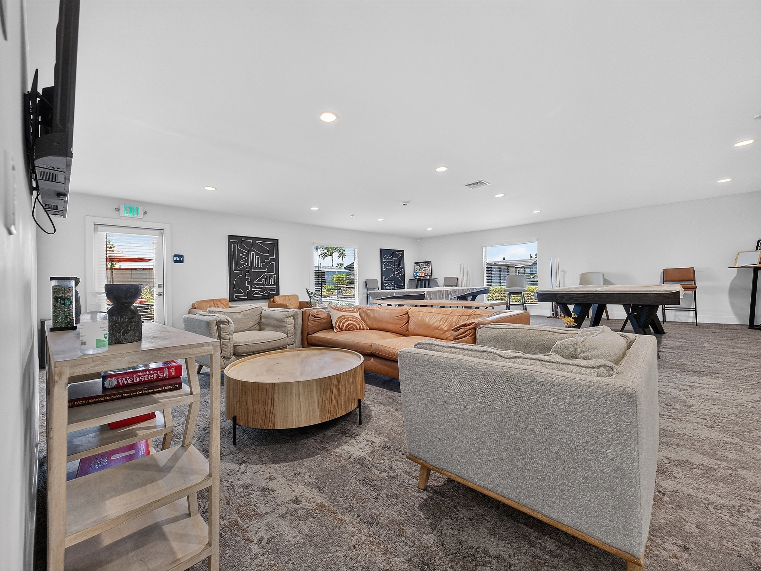 A spacious, well-lit modern living room with light-colored walls and ceiling, multiple ceiling lights, large windows, and contemporary furniture including sofas, chairs, and tables, with art pieces on the walls and decor items.