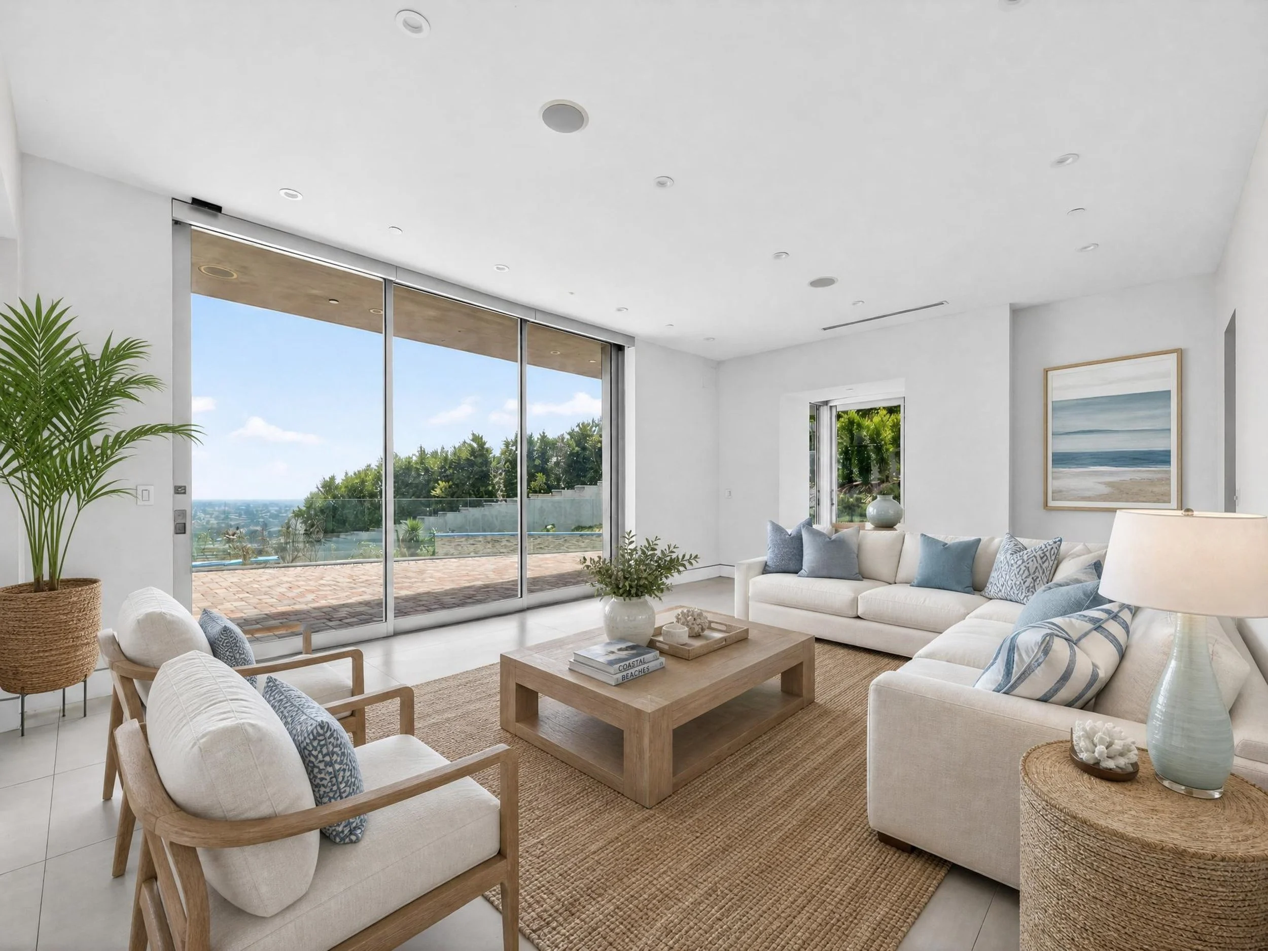 Living room with white sofas, wooden chairs, a wooden coffee table, a large framed beach scene, sliding glass door leading to outdoor patio, potted plant, and modern decor.