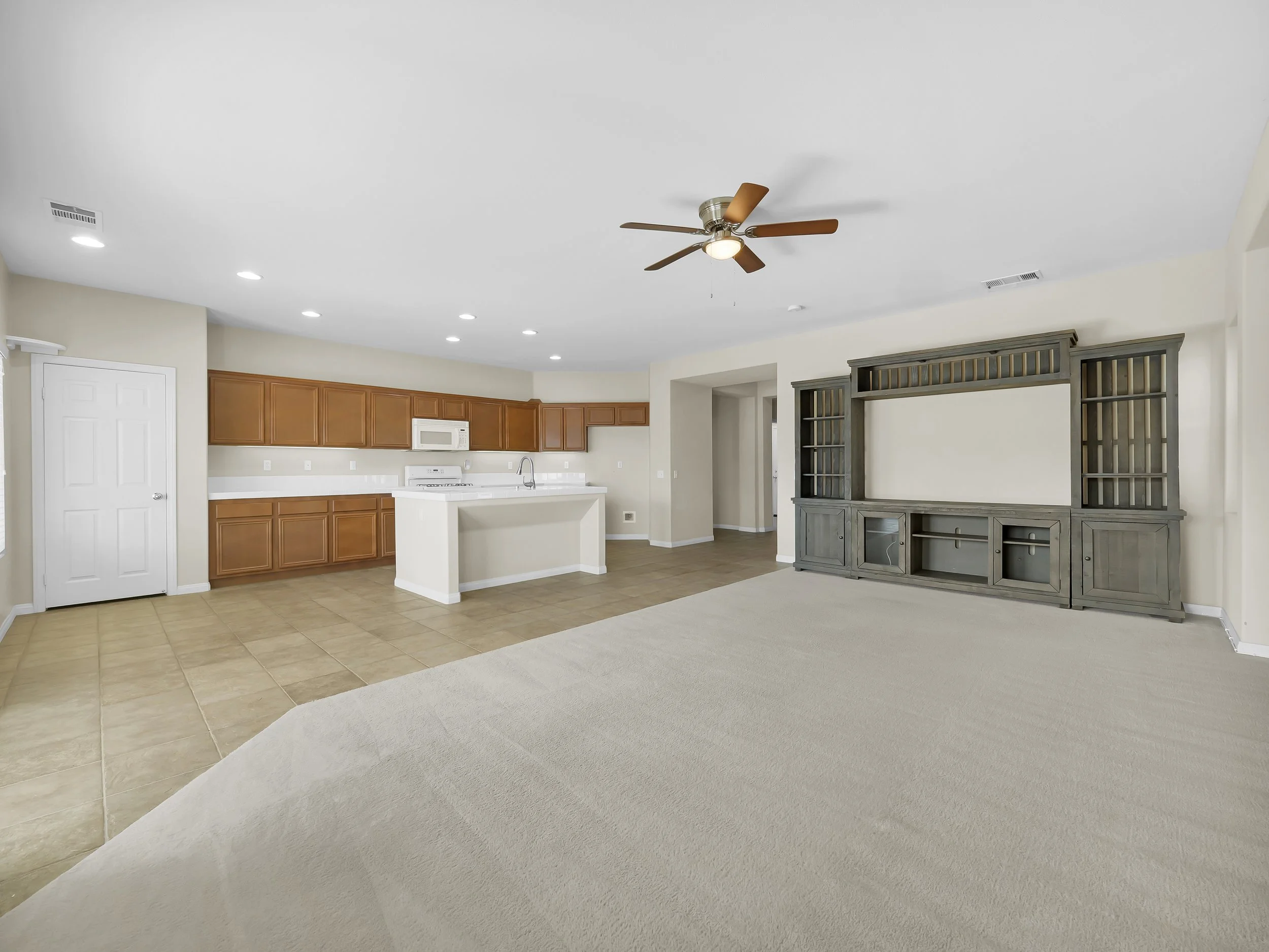 Open-concept kitchen and living room with ceiling fan, recessed lighting, brown cabinets, and gray entertainment center.