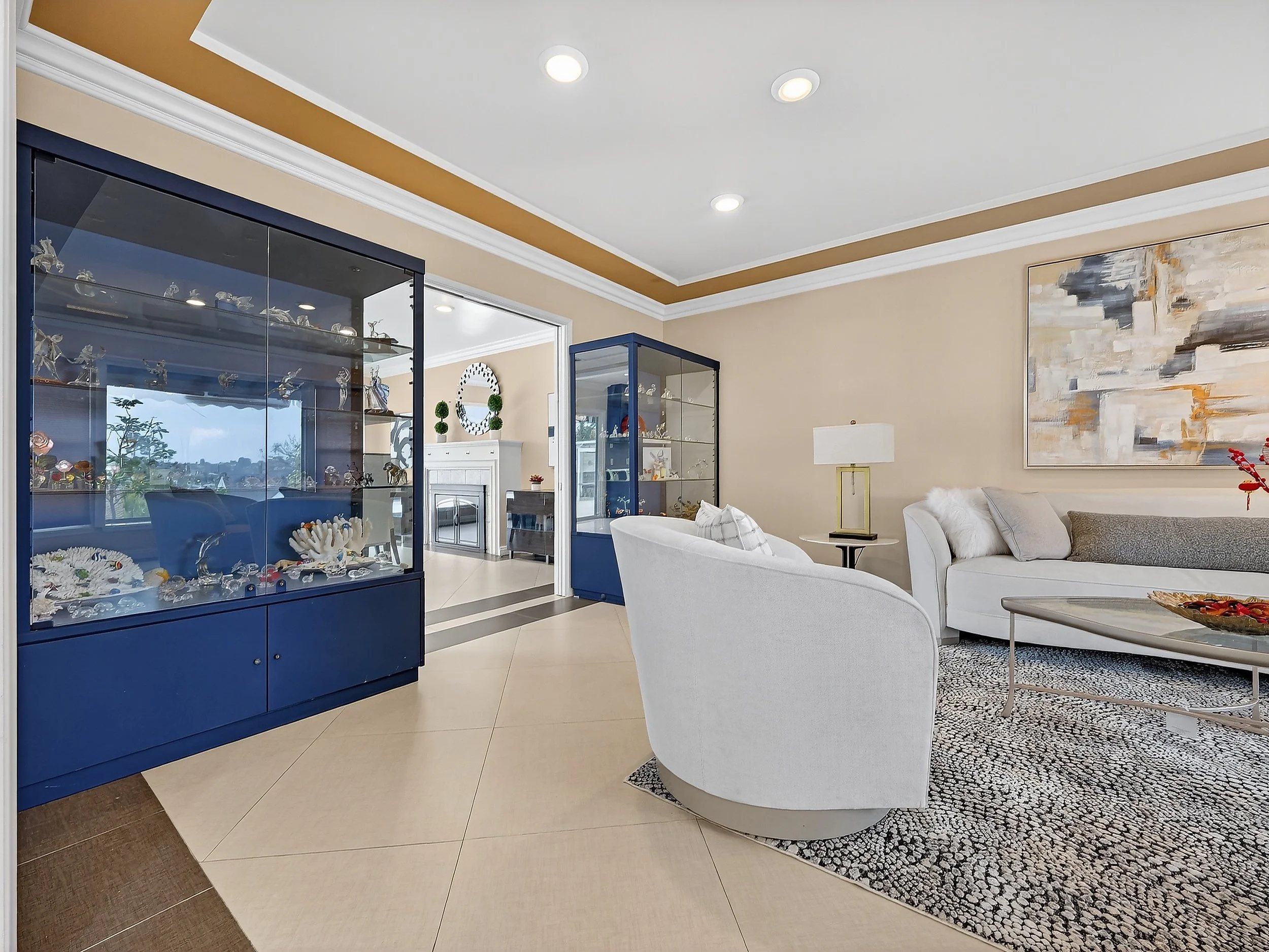 Living room with white couches, a coffee table, a large abstract painting, and display cabinets with collectibles.