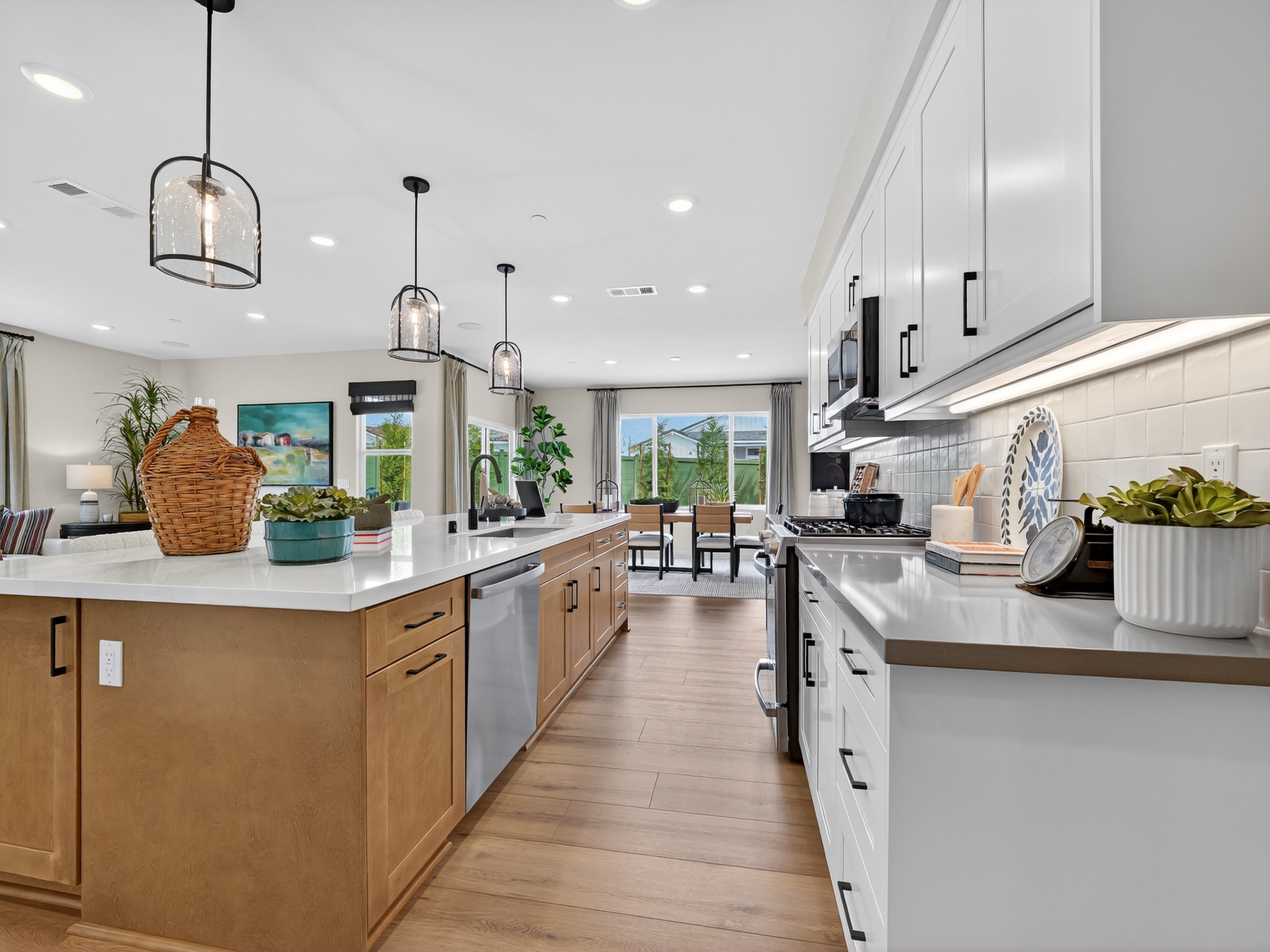 Modern kitchen with white cabinets, a large island with a wooden base, pendant lighting, and large windows showing a backyard.