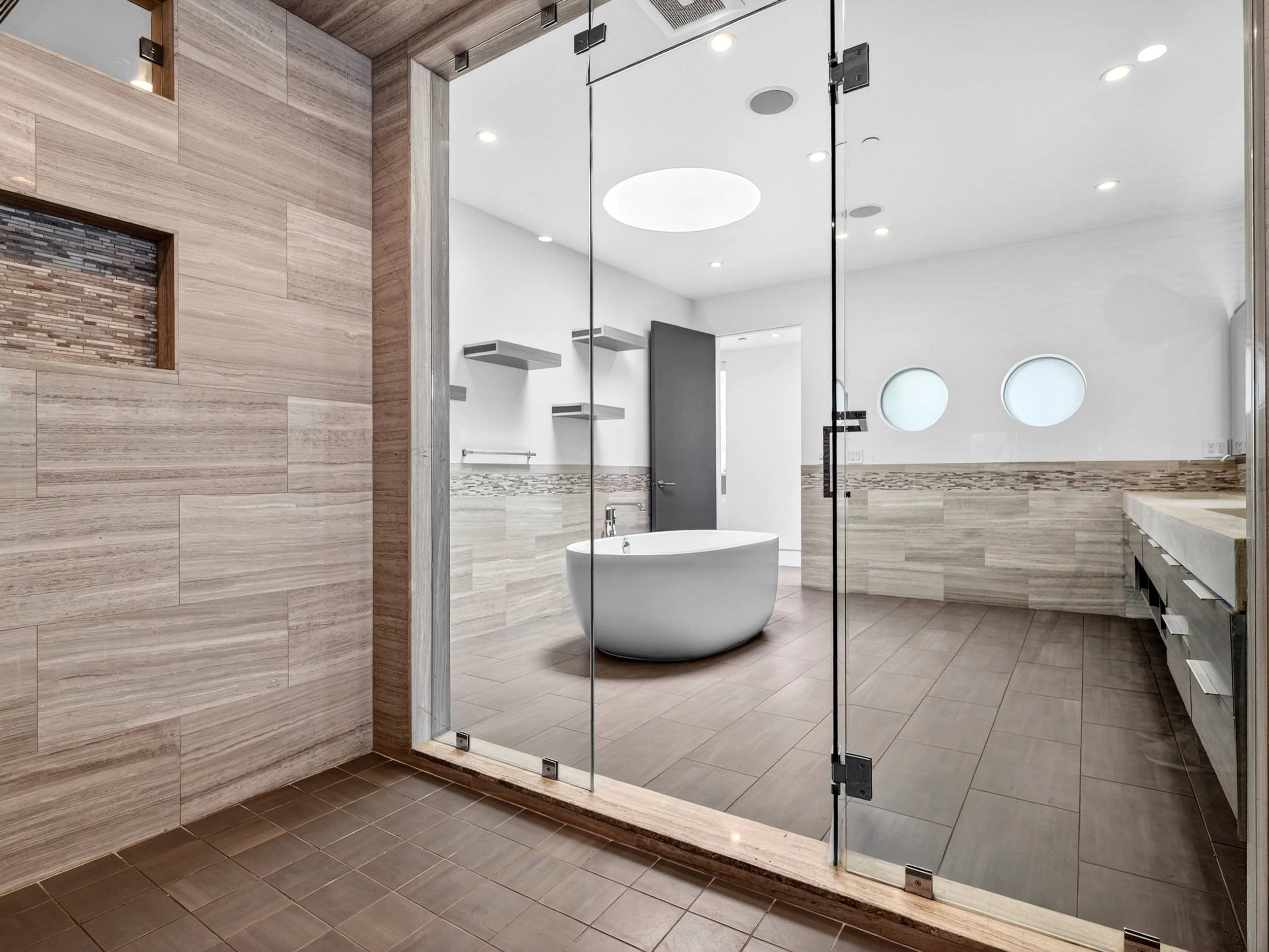 Bathroom with a glass enclosed shower, white bathtub, wood and tile flooring, and modern design elements.